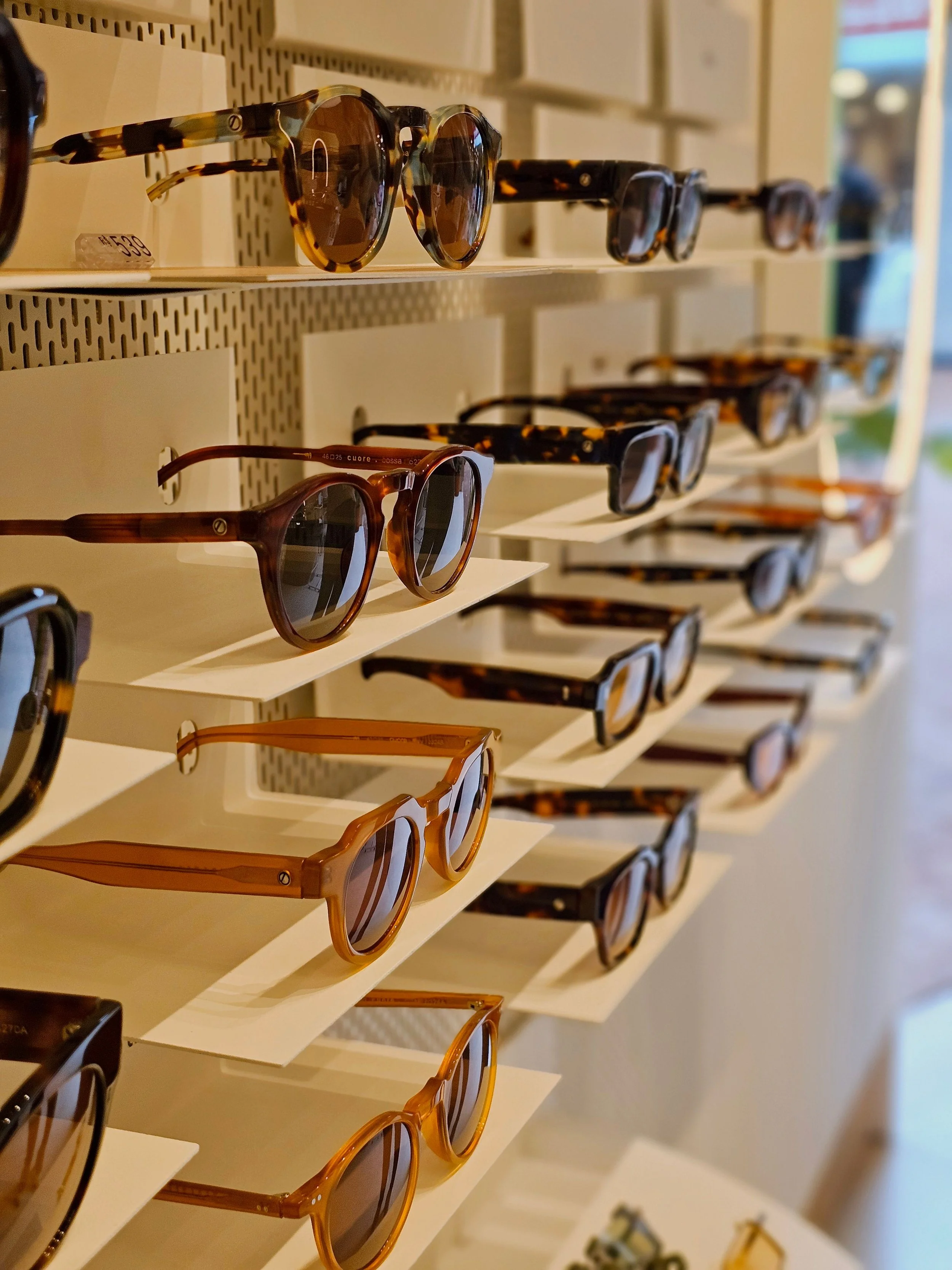 Display of multiple sunglasses on white shelf in an eyewear store