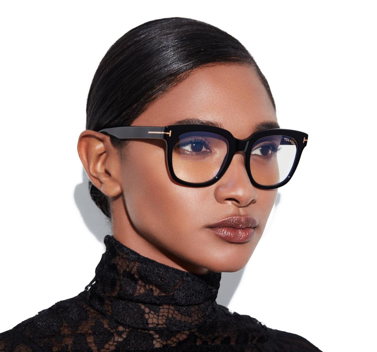 A woman with dark hair and dark eyes wearing black glasses and a black lace top.