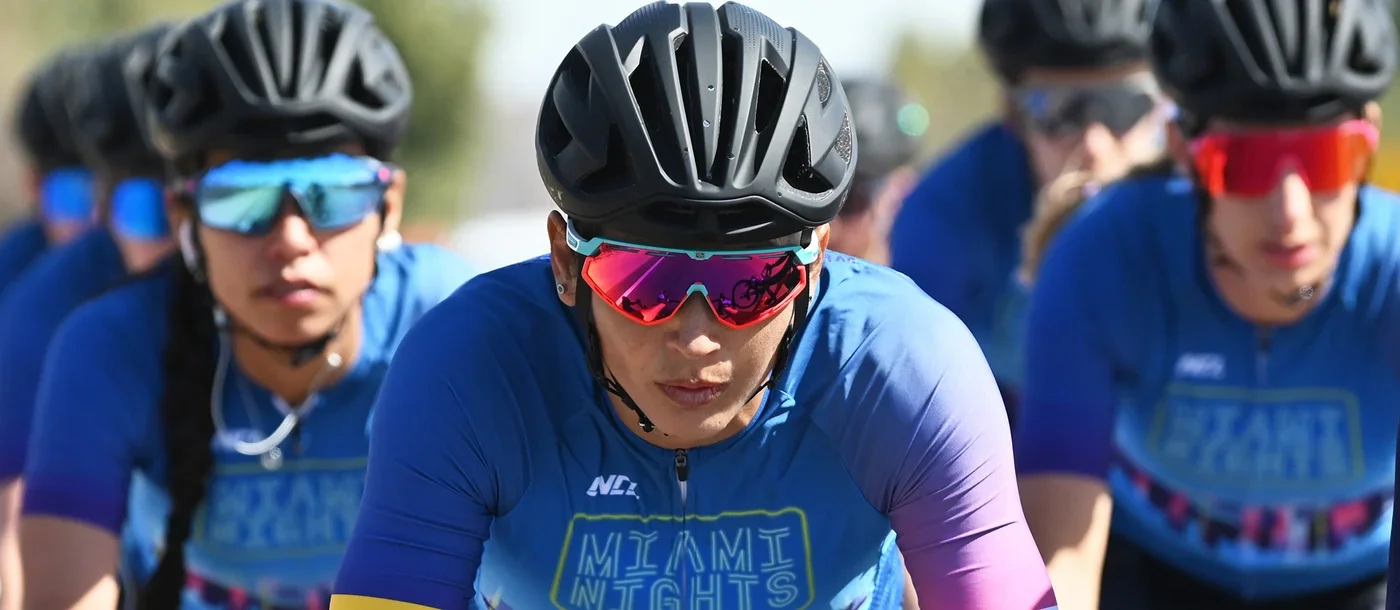 Group of competitive cyclists in blue jerseys and helmets riding outdoors during daytime.