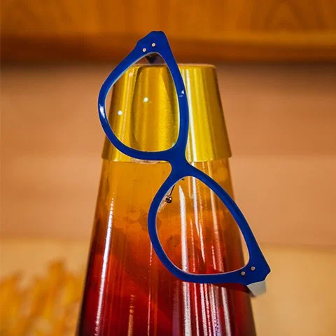 A colorful lava lamp with red, orange, and yellow wax inside, topped with blue sunglasses resting on it.