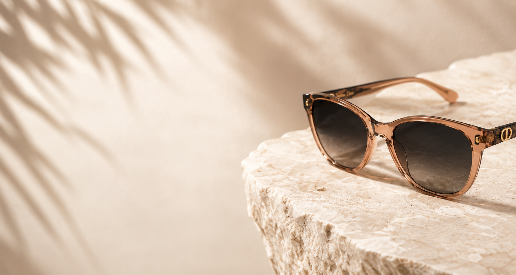 A pair of sunglasses with a pinkish-brown frame and dark lenses resting on a textured beige stone surface with soft shadow.