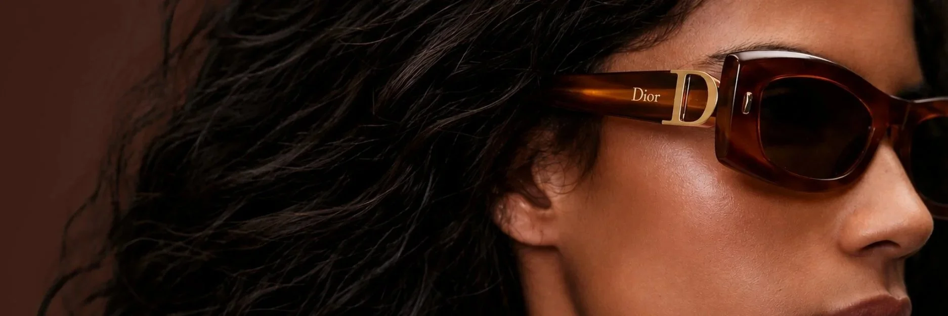 Close-up of a woman wearing brown Dior sunglasses with dark wavy hair.