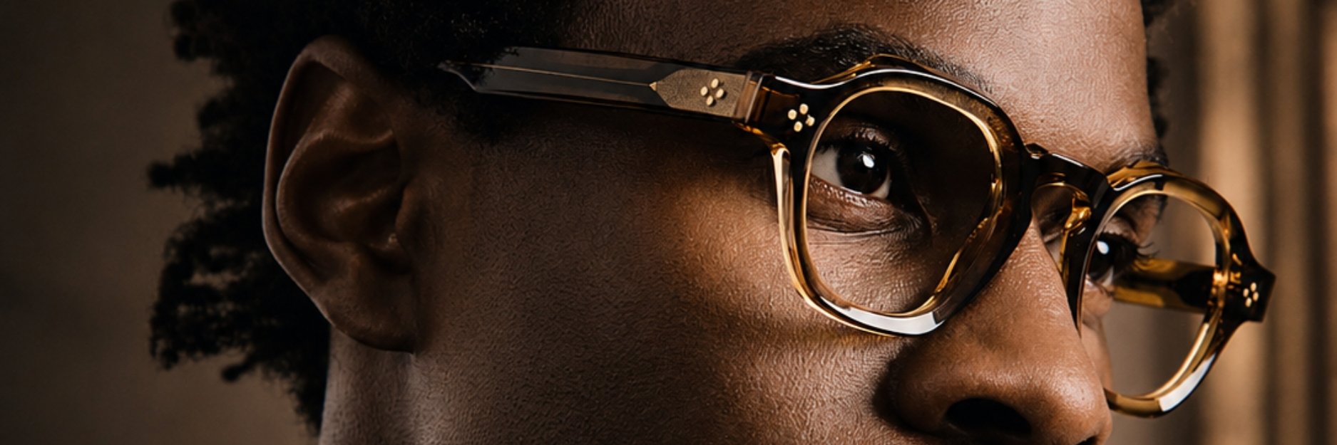 Close-up of a person wearing tortoise shell glasses, showing the right eye and part of the face, with natural textured skin and short curly hair.