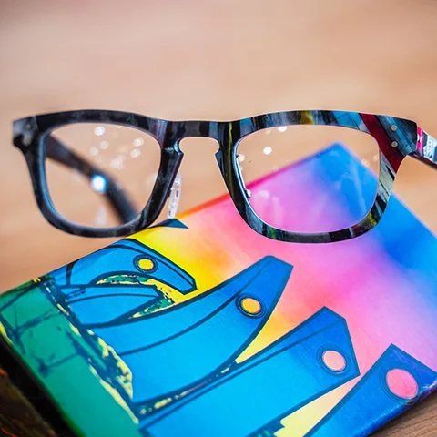 Close-up of a pair of colorful sunglasses resting on a rainbow-colored skateboard.