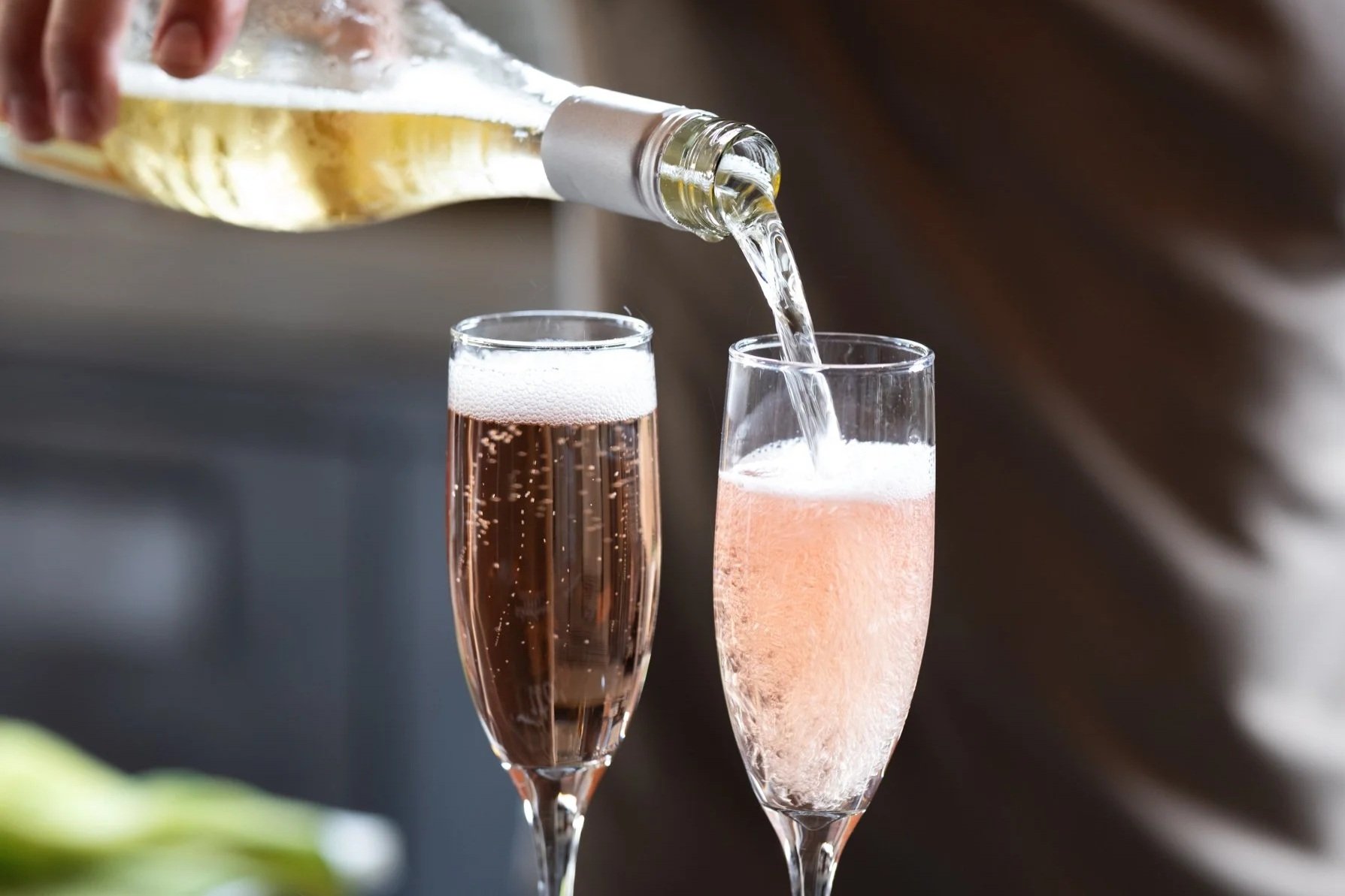 A person is pouring white wine into a pink sparkling wine glass, with another pink sparkling wine glass already filled nearby.