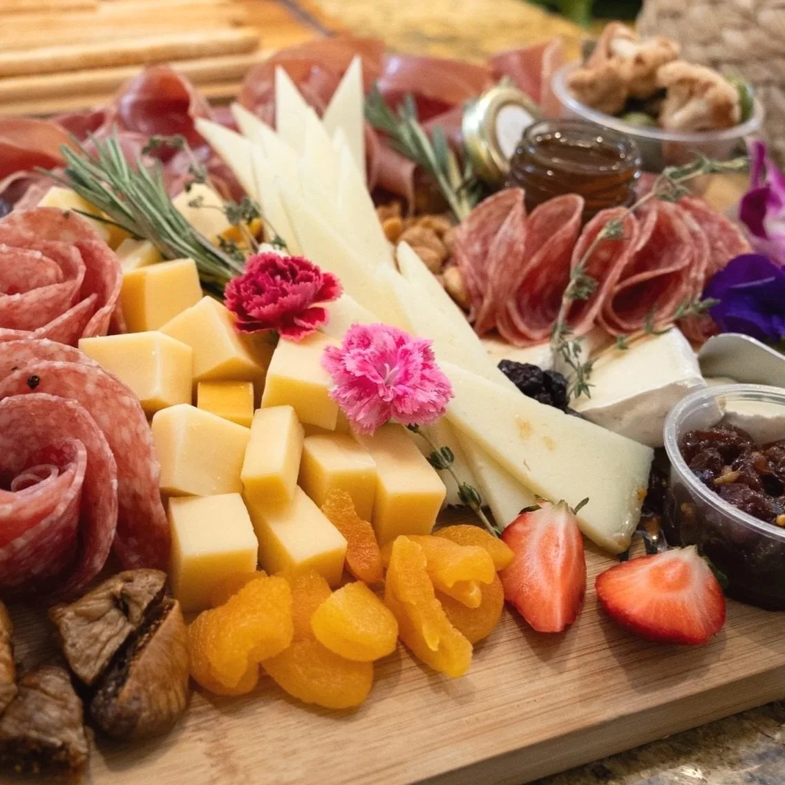 Cheese, cured meats, strawberries, walnuts, fruit preserves, and herbs on a cheese platter.