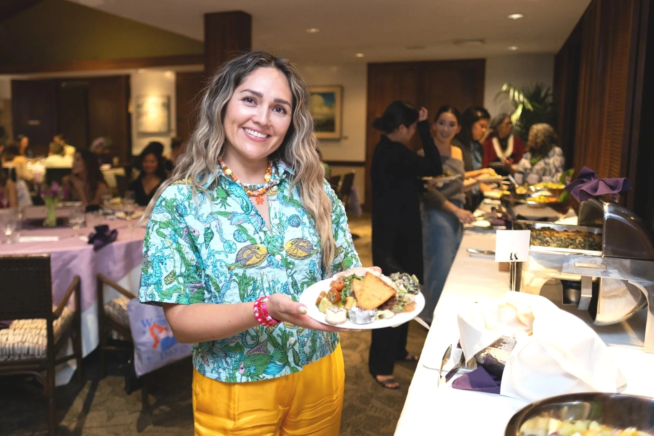 A woman holding a plate of food at a buffet during a social event in a restaurant or banquet hall.