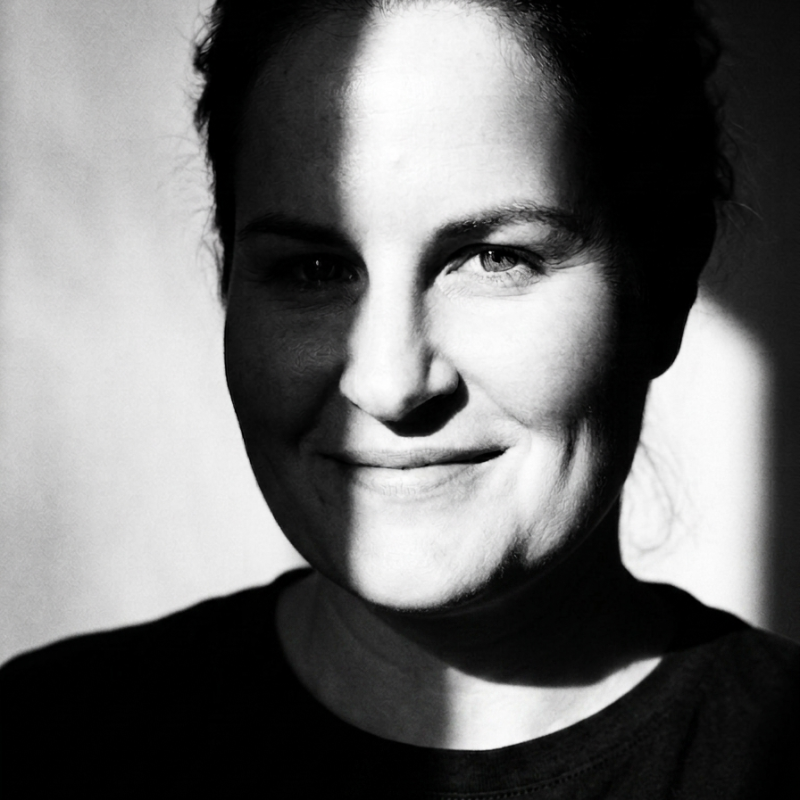 Black and white portrait of a woman with a slight smile, half of her face illuminated by light, with shadows on the other side.