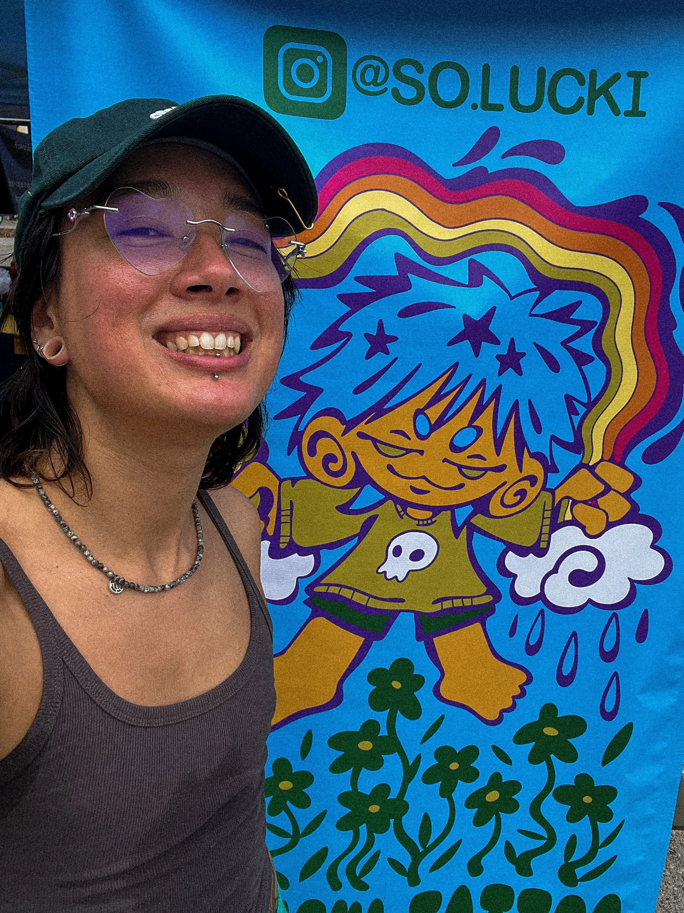 A person wearing a black cap, heart-shaped sunglasses, and a black tank top
