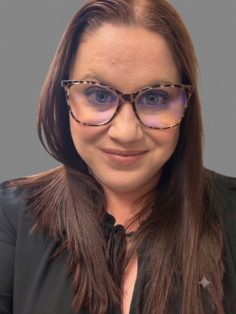A woman with shoulder-length brown hair wearing glasses with tortoise shell frames, smiling, against a plain gray background.