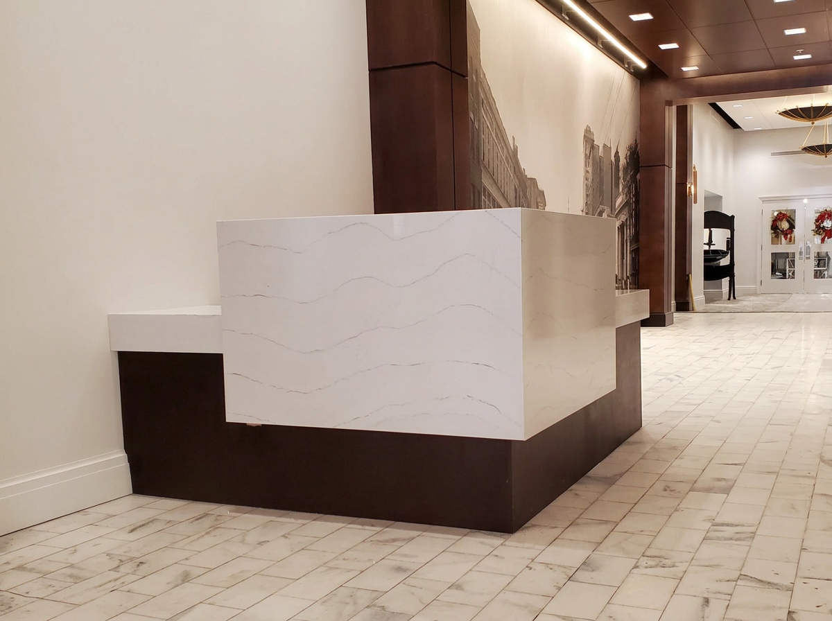 Modern interior reception desk with white marble top, dark wood base, and a large mural of city buildings in the background.