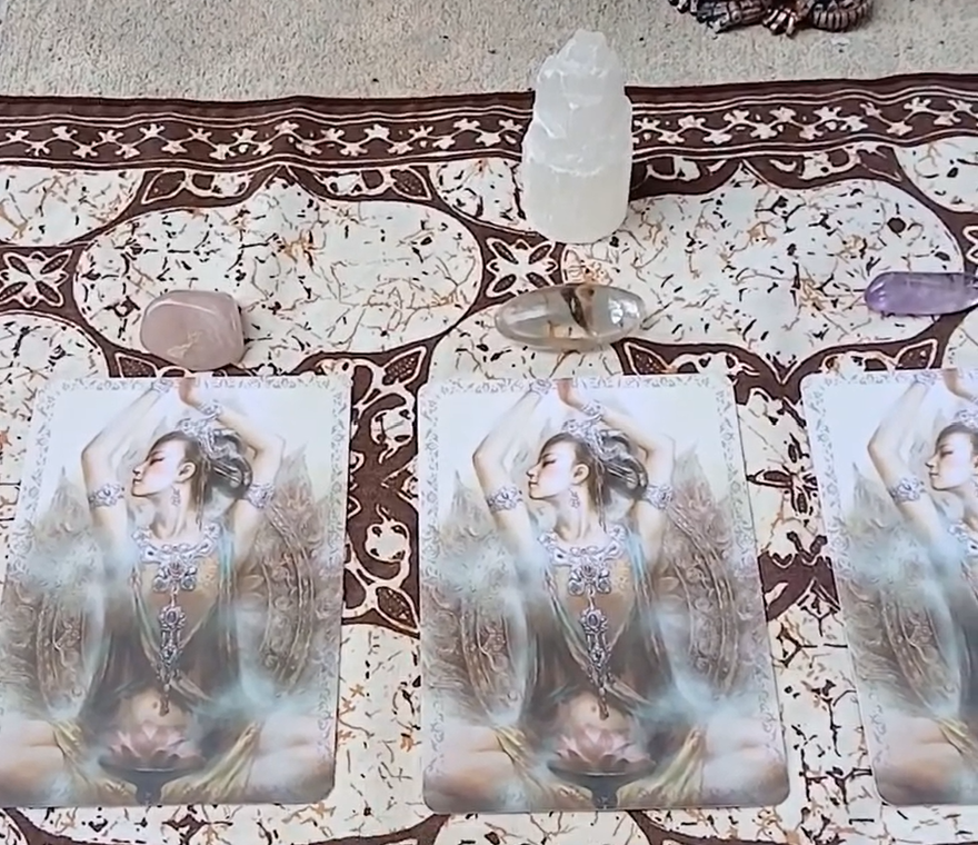 Three tarot cards featuring a woman with golden hair and ornate jewelry, laid out on a decorative cloth with crystals on top.