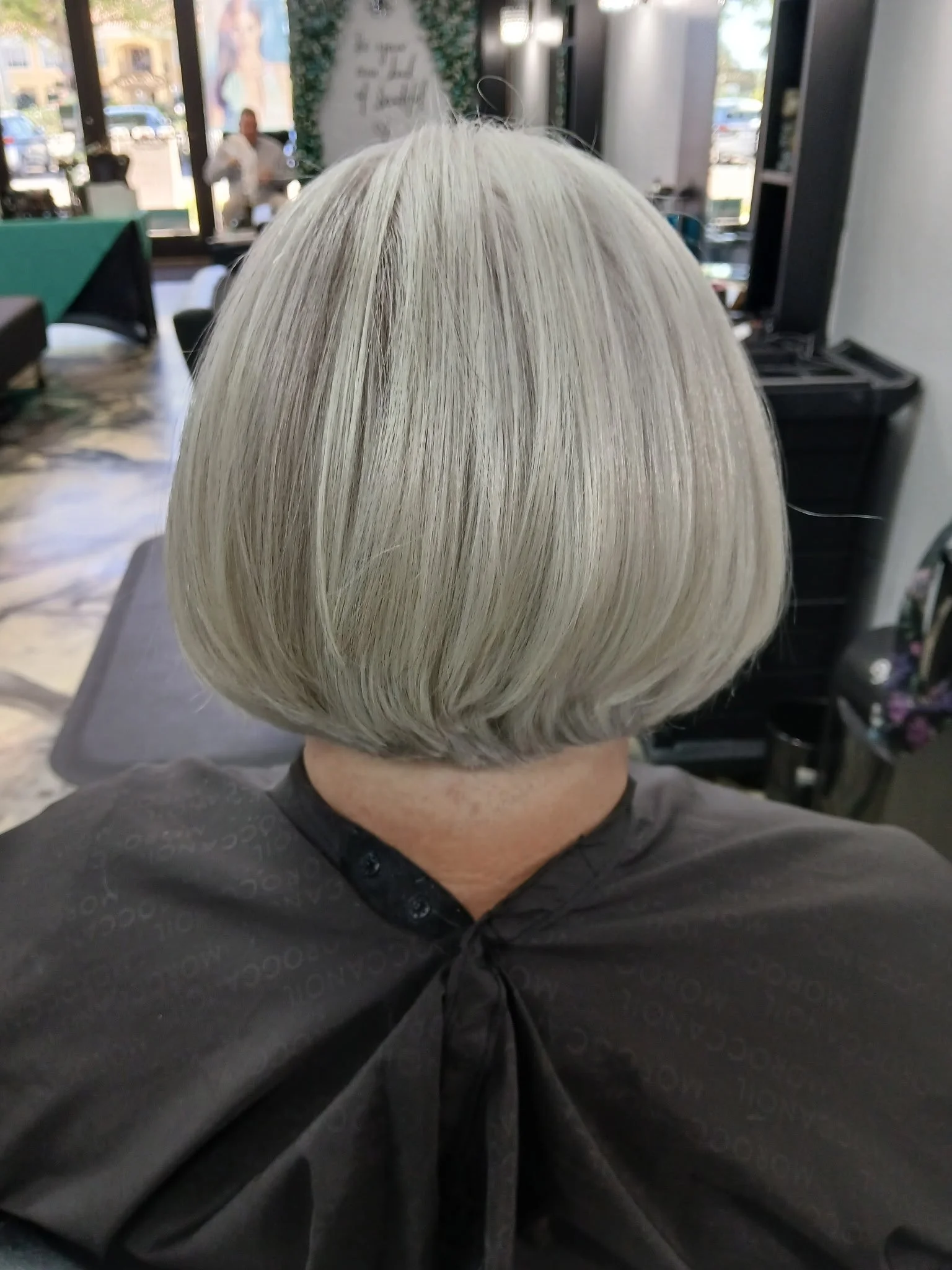 Back view of a woman with a short, platinum blonde bob haircut in a hair salon.