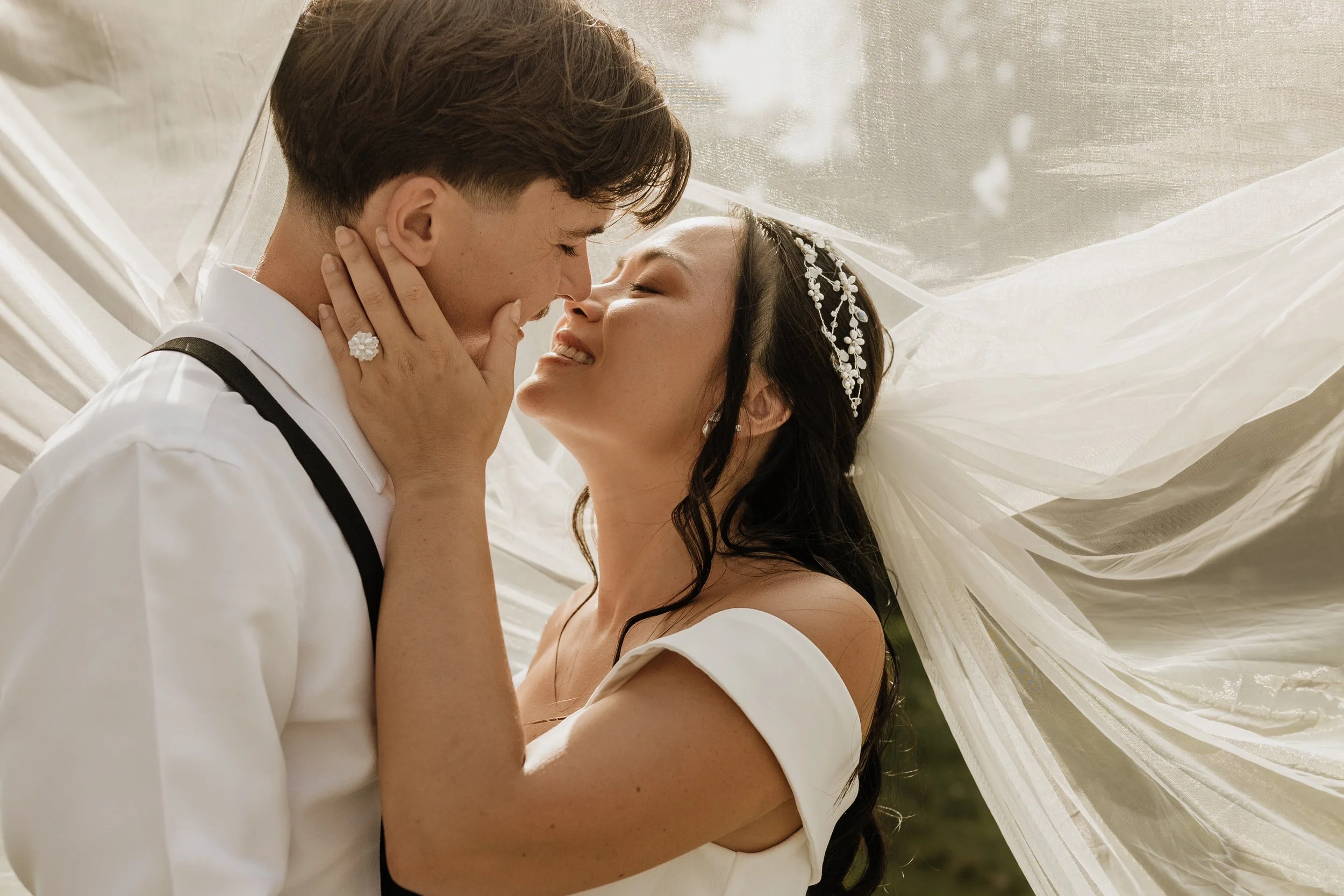 Un couple en robe de mariée et costume en train de s'embrasser sous un voile de mariée lors d'une séance photo en bretagne
