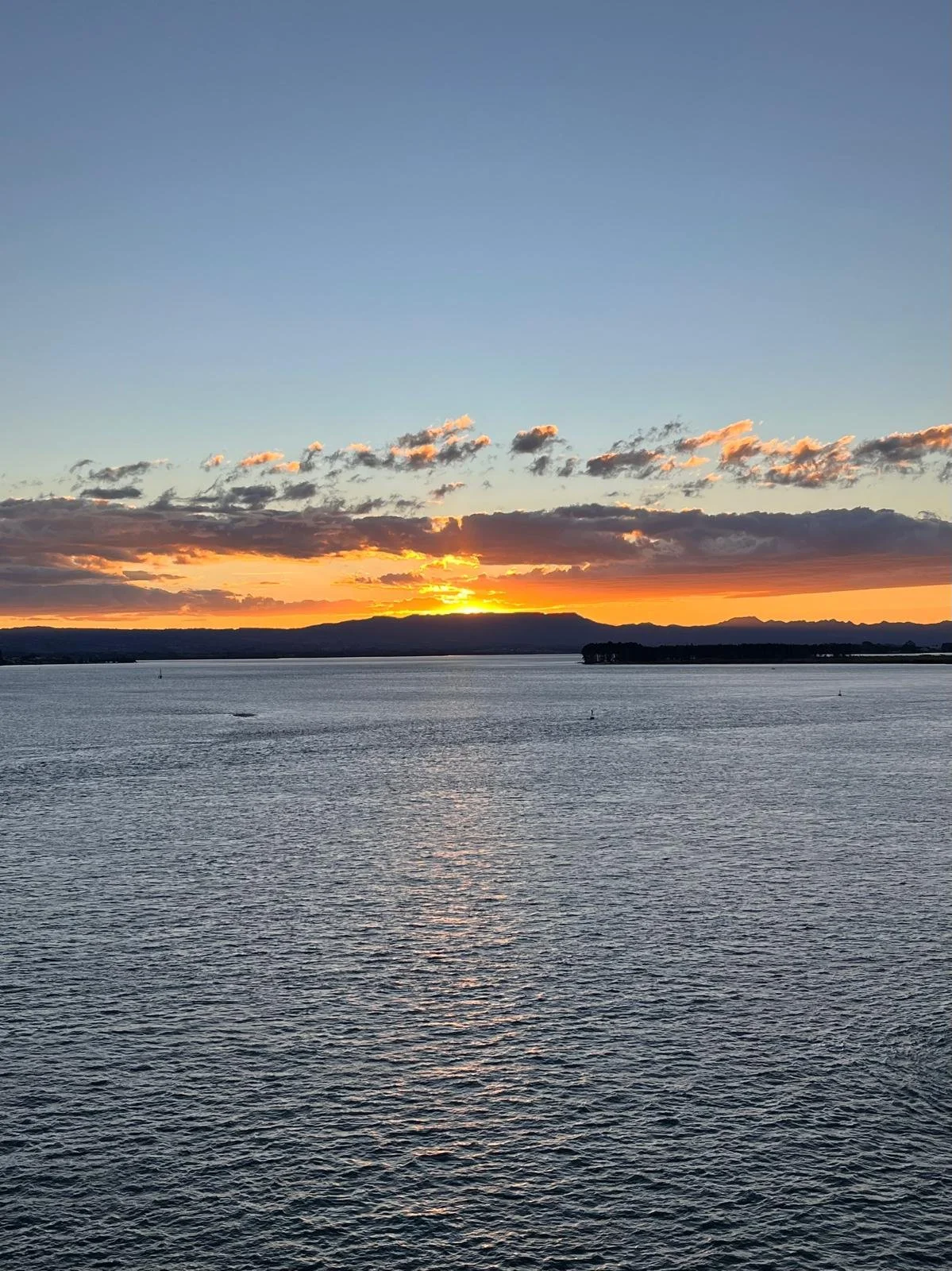 A sunset over a large body of water with mountains in the background and clouds in the sky.