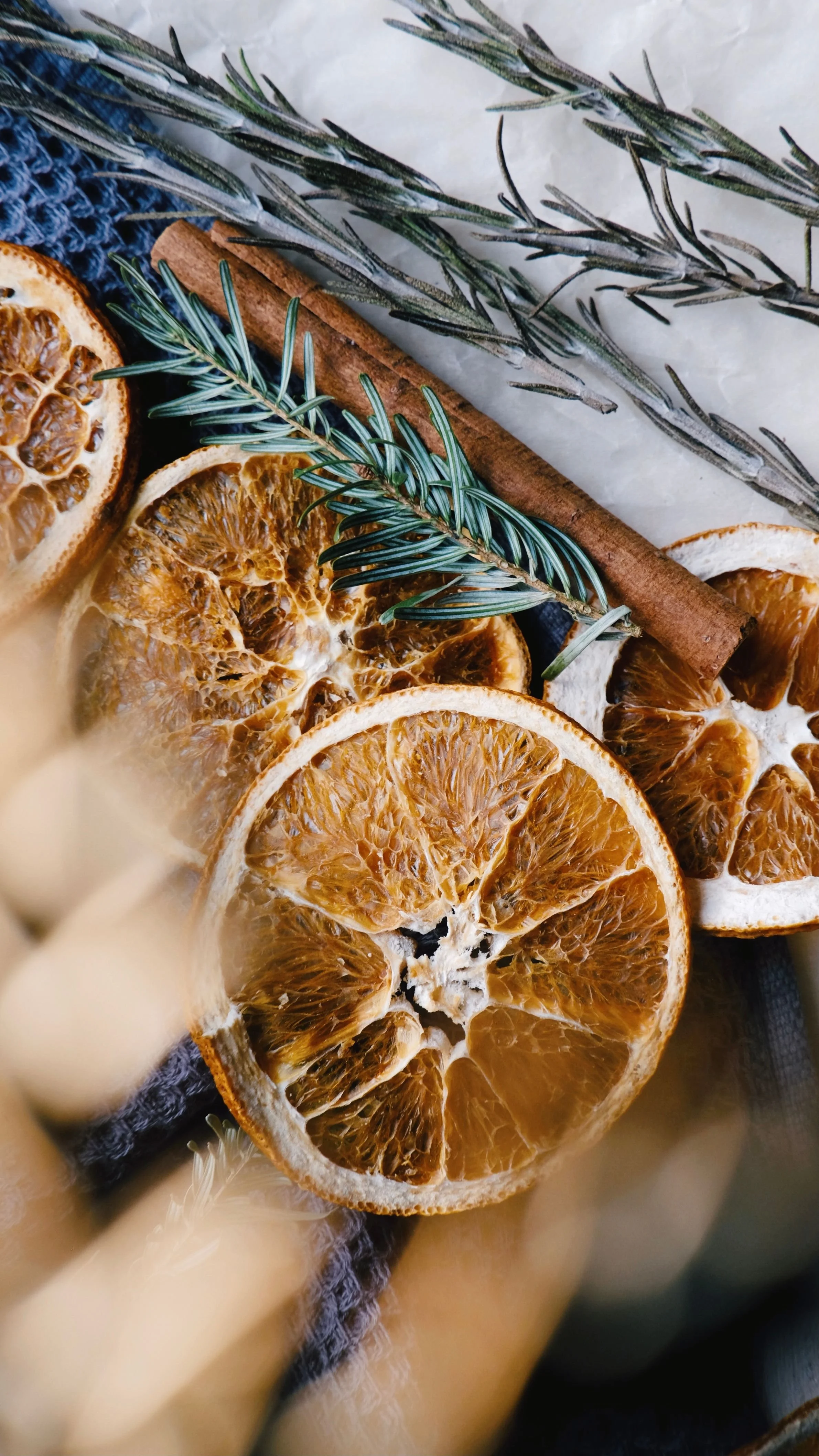 Dried orange slices, cinnamon sticks, and sprigs of rosemary arranged on fabric with a blurred background.