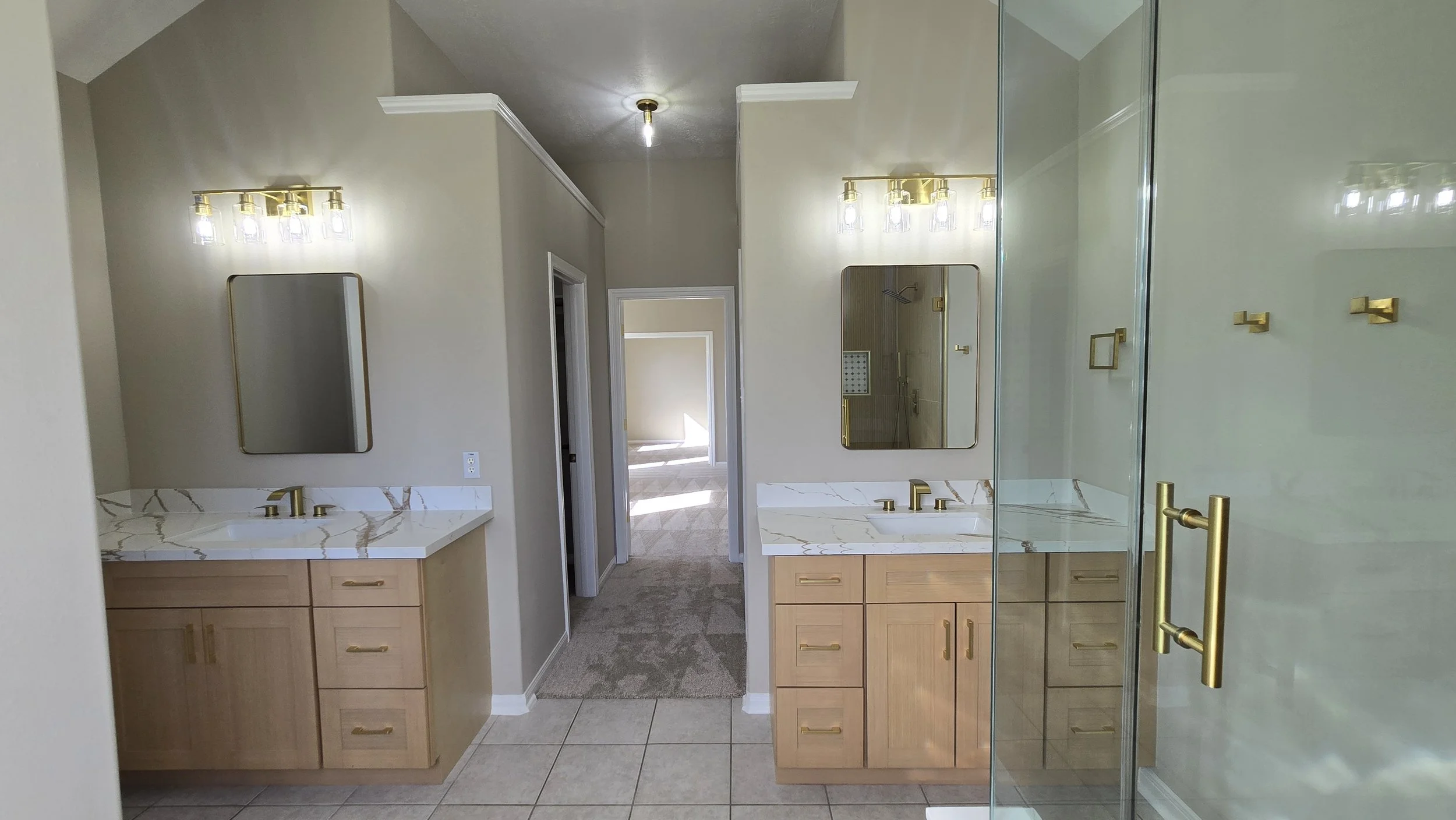 TurnKey Roofing & Restoration — A newly renovated / remodeled bathroom with double vanities featuring marble countertops and wooden cabinets, two mirrors, and a glass shower enclosure with brass hardware. Houston, Texas