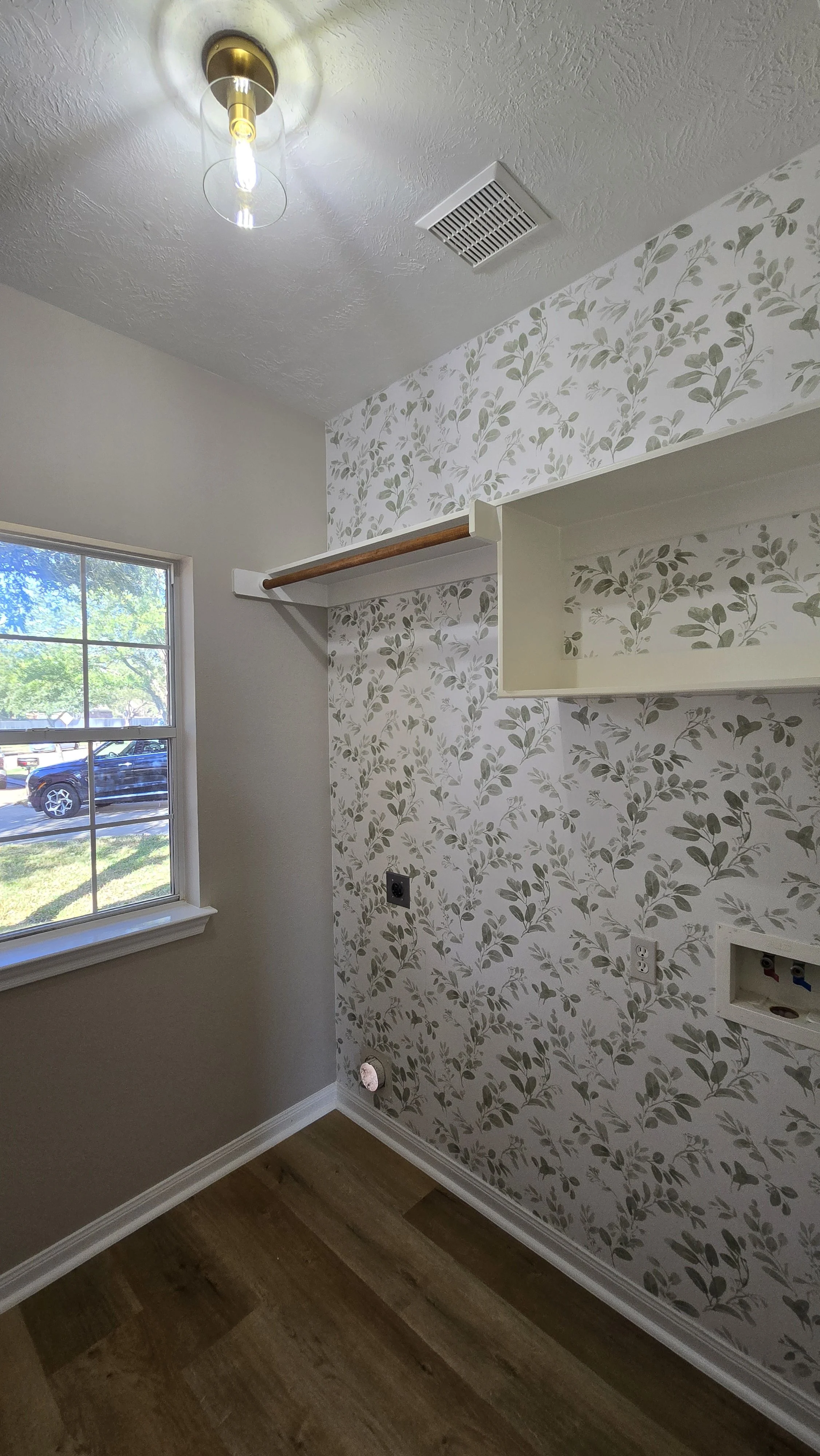 TurnKey Roofing & Restoration — Empty room with a window, floral wallpaper, a ceiling light, and open space for a washer and dryer.