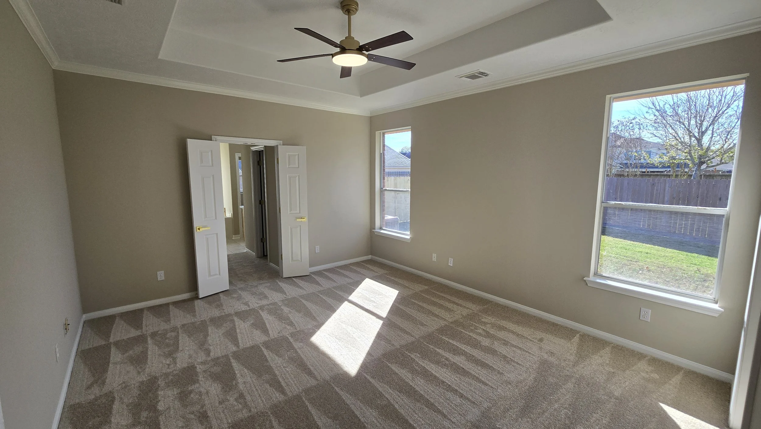 TurnKey Roofing & Restoration — A newly renovated / remodeled bedroom with beige walls, carpeted floor, two windows showing a fenced backyard, and a ceiling fan. Houston, Texas