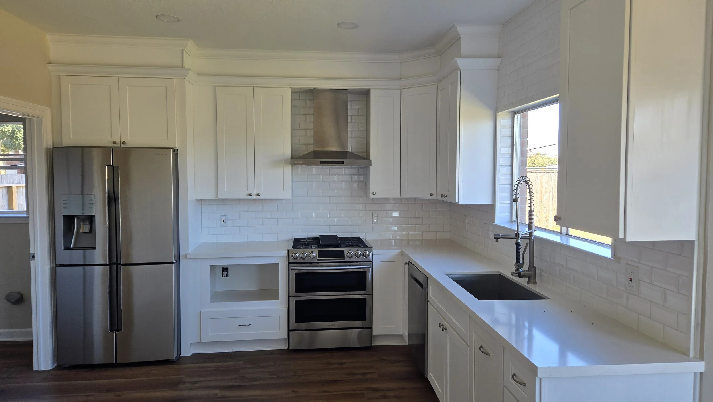 TurnKey Roofing & Restoration — A newly renovated / remodeled modern kitchen with white cabinets, stainless steel refrigerator, gas stove, black sink, and windows letting in natural light. Houston, Texas
