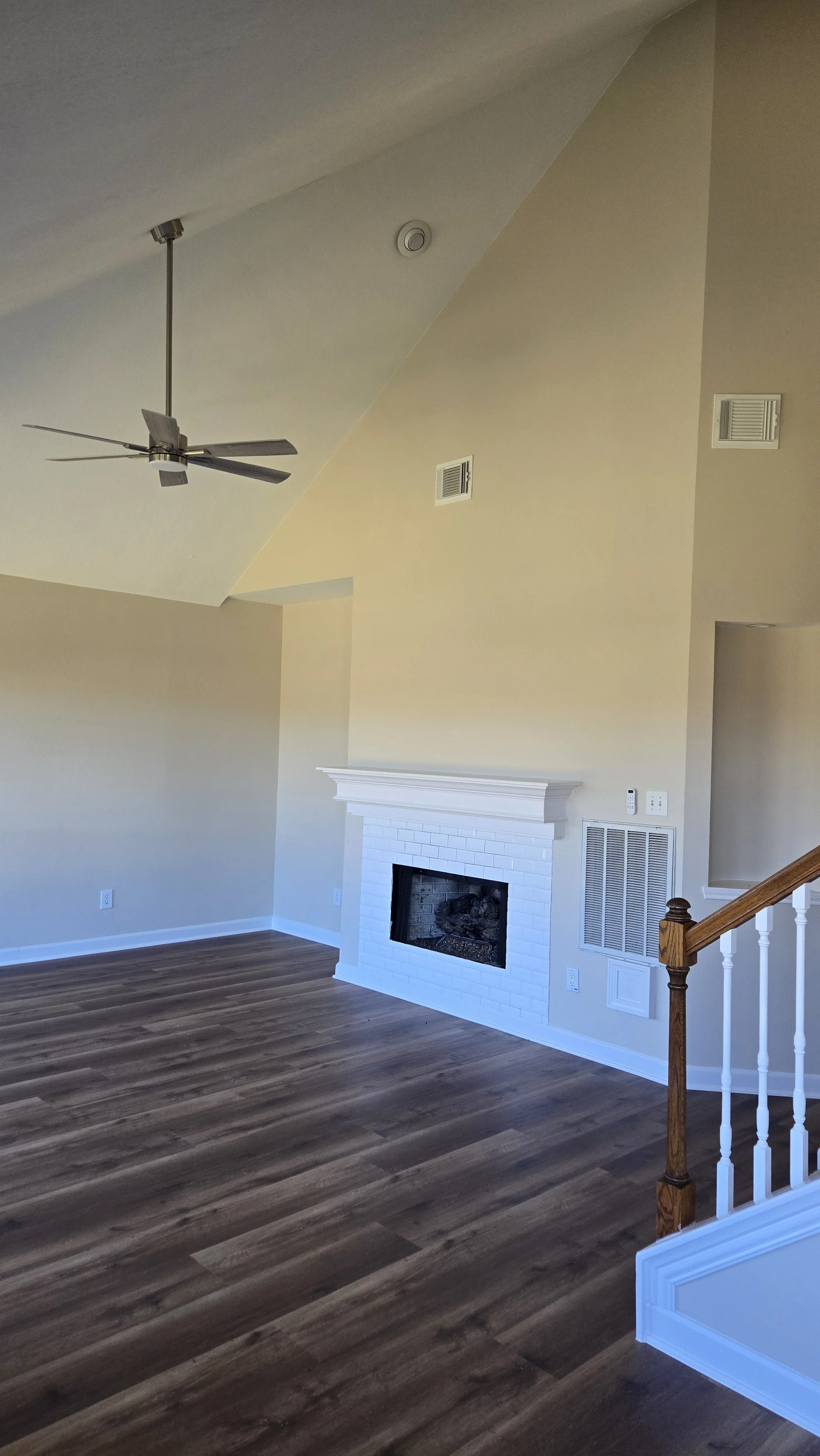 TurnKey Roofing & Restoration — A newly renovated / remodeled living room with hardwood floors, a white brick fireplace with a white mantel, a ceiling fan, and beige walls. Houston, Texas