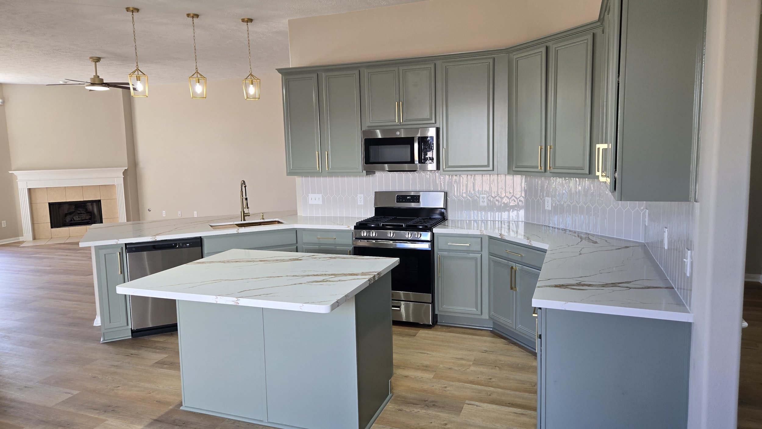 TurnKey Roofing & Restoration — A newly renovated / remodeled modern kitchen with light green blue cabinets, white and gold marble countertop, stainless steel appliances, and pendant lighting fixtures. Houston, Texas