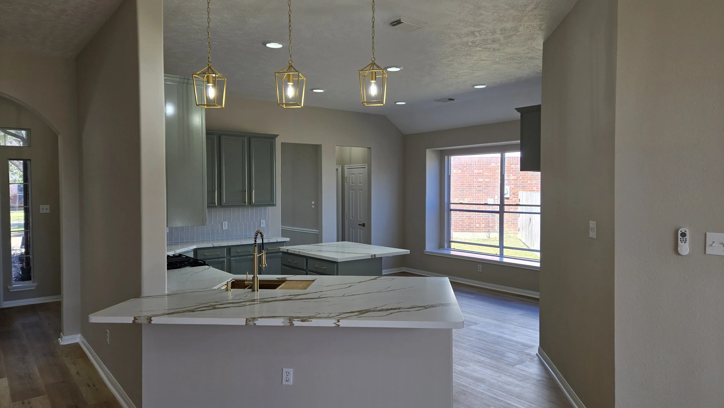 TurnKey Roofing & Restoration — A newly renovated / remodeled modern kitchen with light green blue cabinets, white and gold marble countertop, stainless steel appliances, and pendant lighting fixtures. Houston, Texas