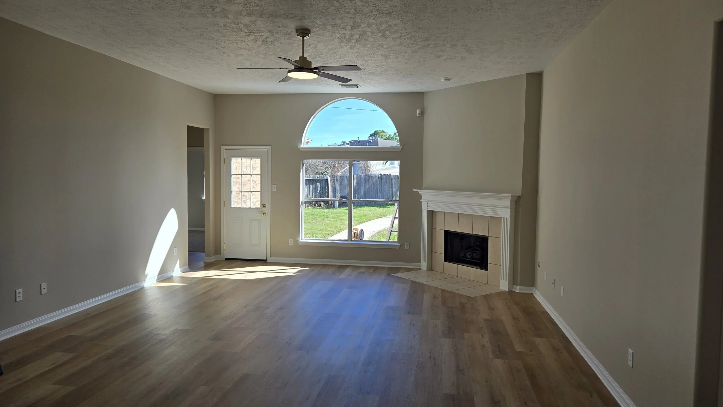 	
TurnKey Roofing & Restoration — A newly renovated / remodeled living room with hardwood floors, light beige walls, a ceiling fan, a fireplace, and large windows. Houston, Texas