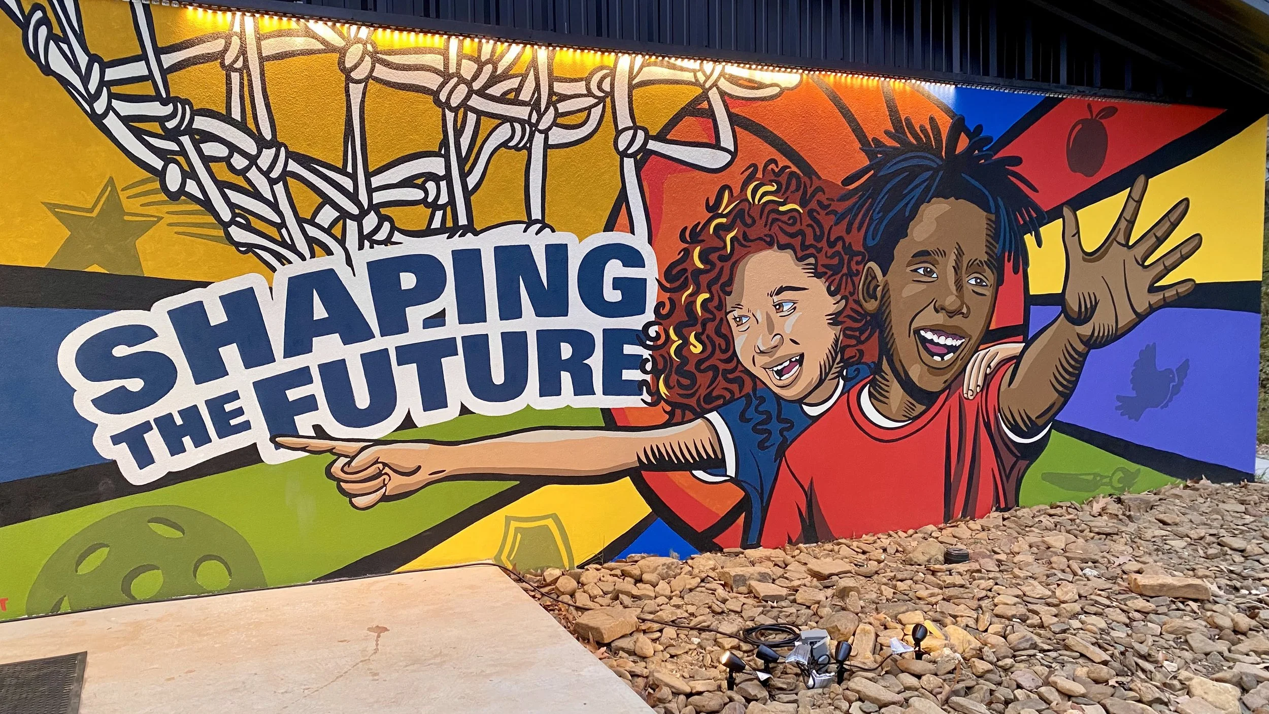 Colorful mural featuring two smiling children reaching out with their arms, with the words "Shaping the Future" on the mural.