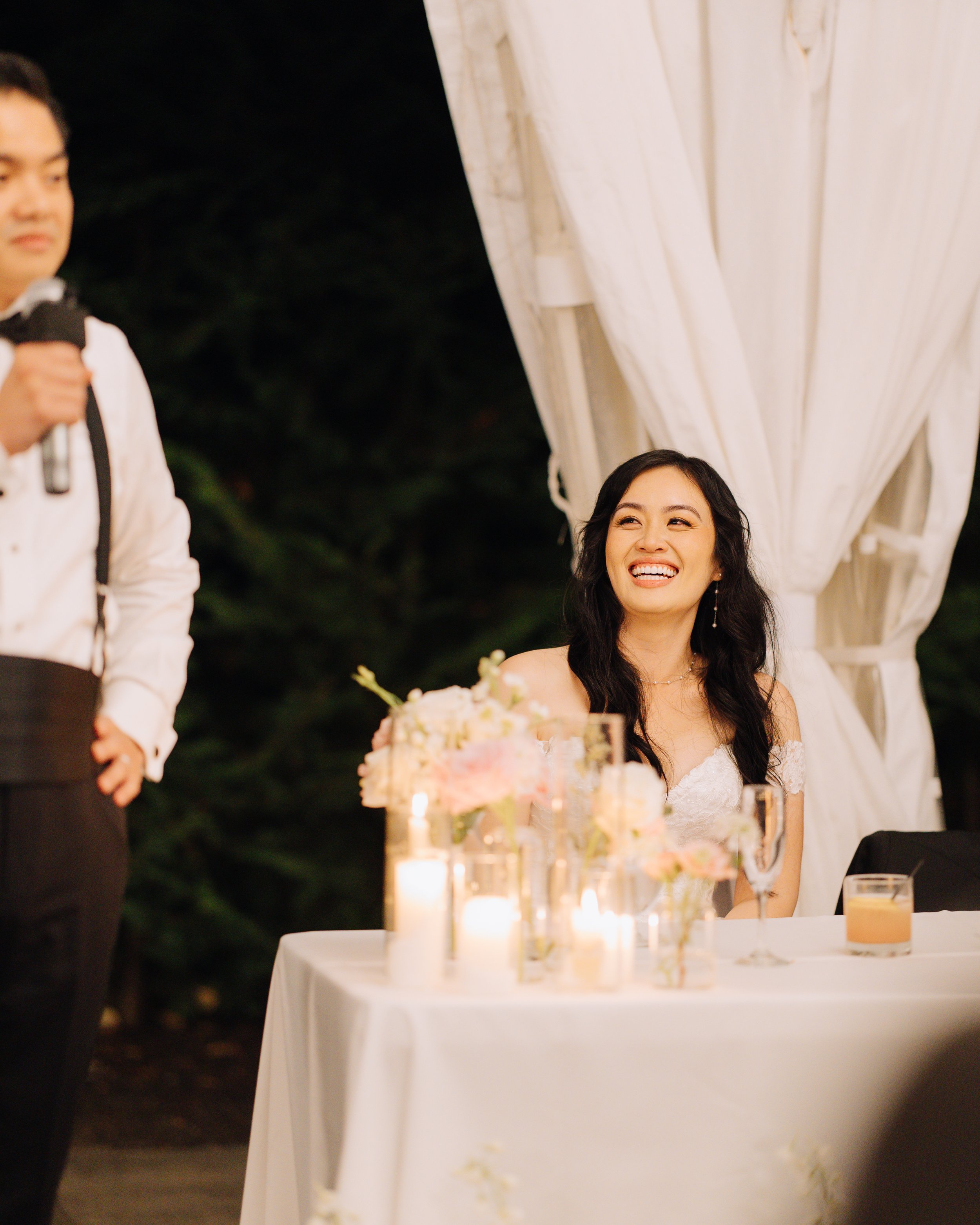 Bride smiling at the reception table during an evening wedding celebration.