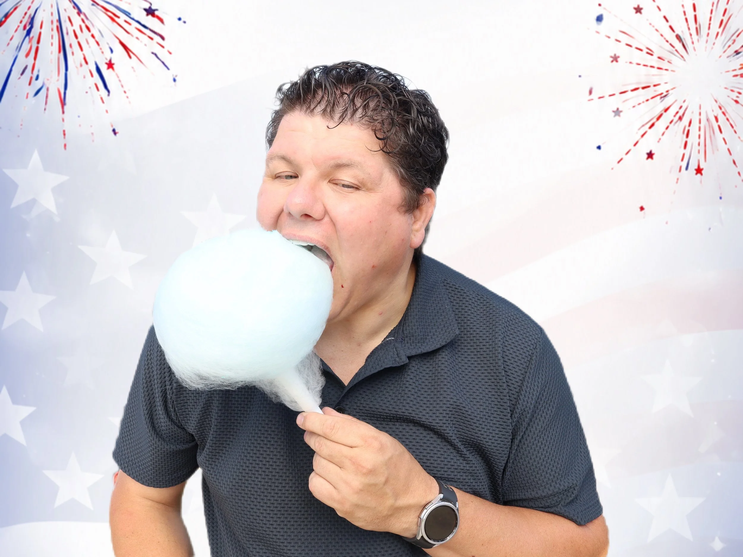 A man is holding and about to eat cotton candy in front of a patriotic background with red, white, and blue fireworks and stars.