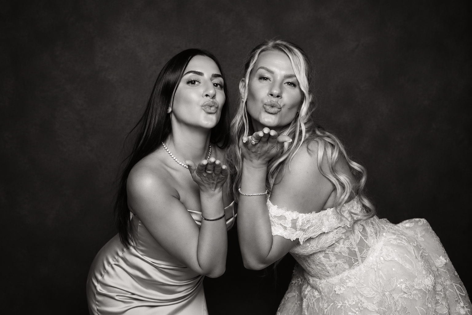 Bride and guest posing for a playful black-and-white studio portrait at a wedding.