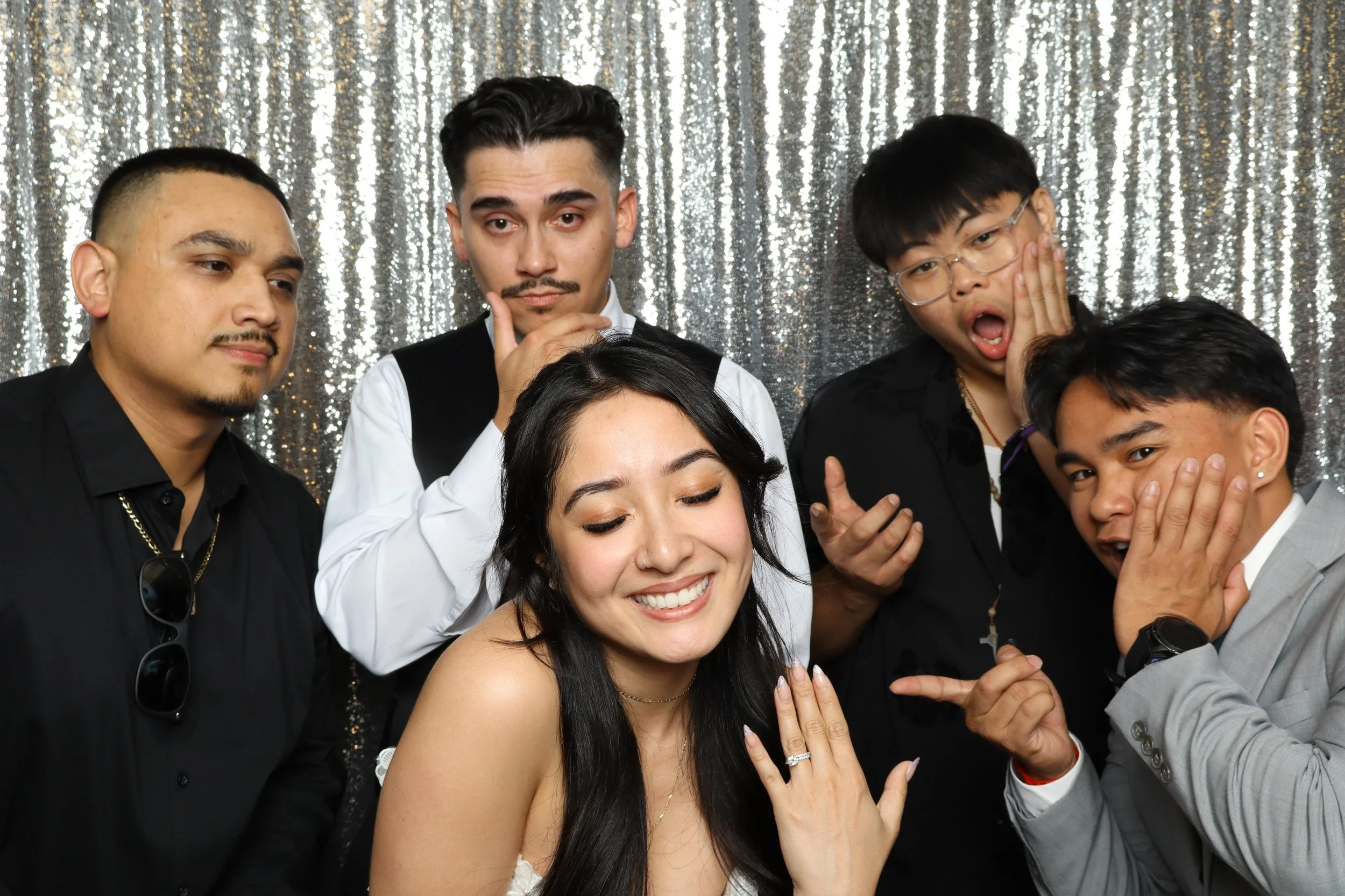 Group of five young adults posing against a shiny, silver, sequin backdrop, showing various facial expressions and gestures.