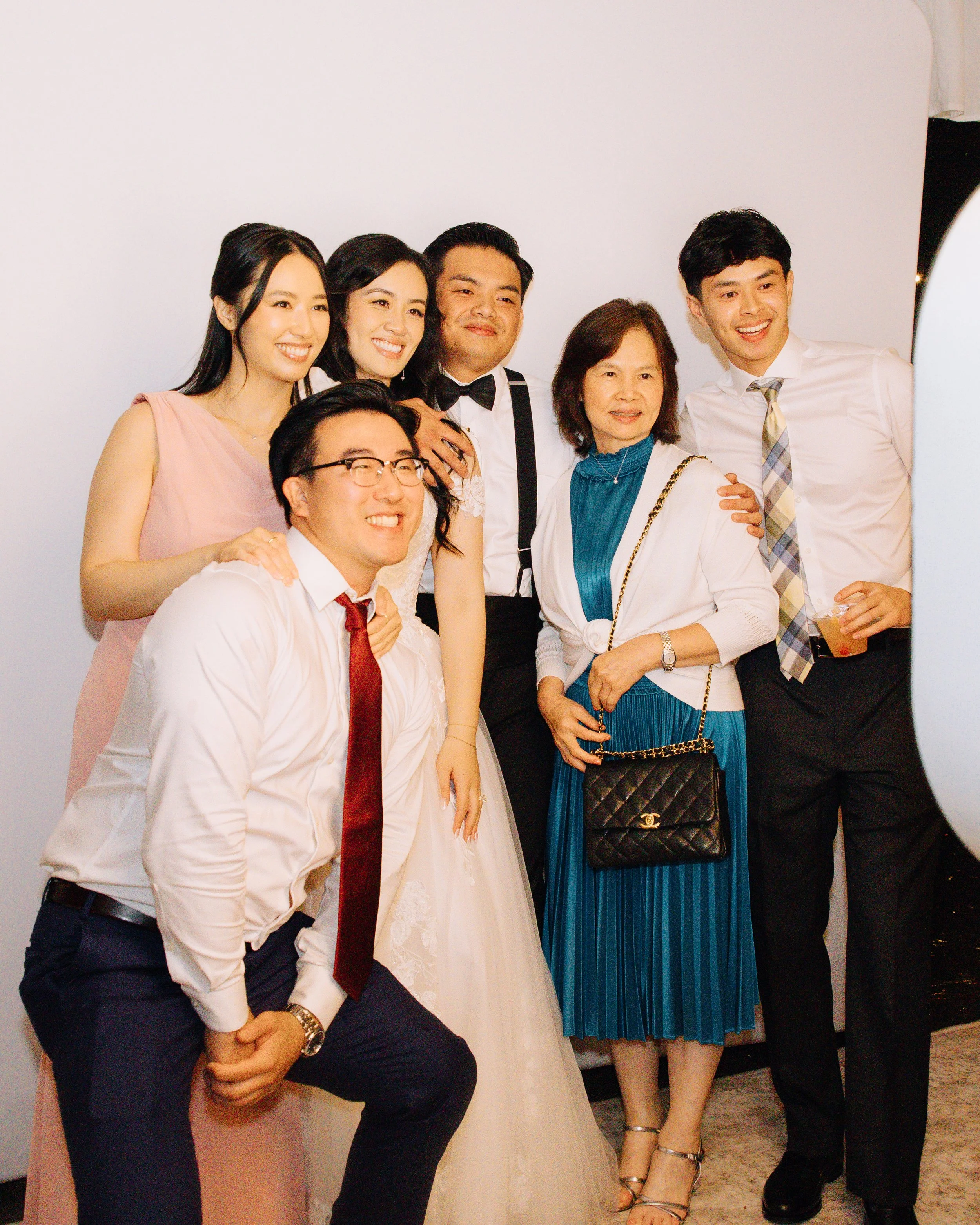 Large group of wedding guests crowding into the photo booth with playful props.