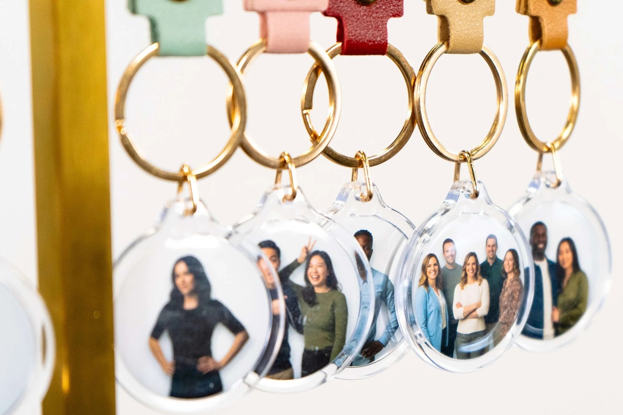 Close-up of several keychains hanging on a yellow display, with each keychain featuring a round photo of diverse smiling people.
