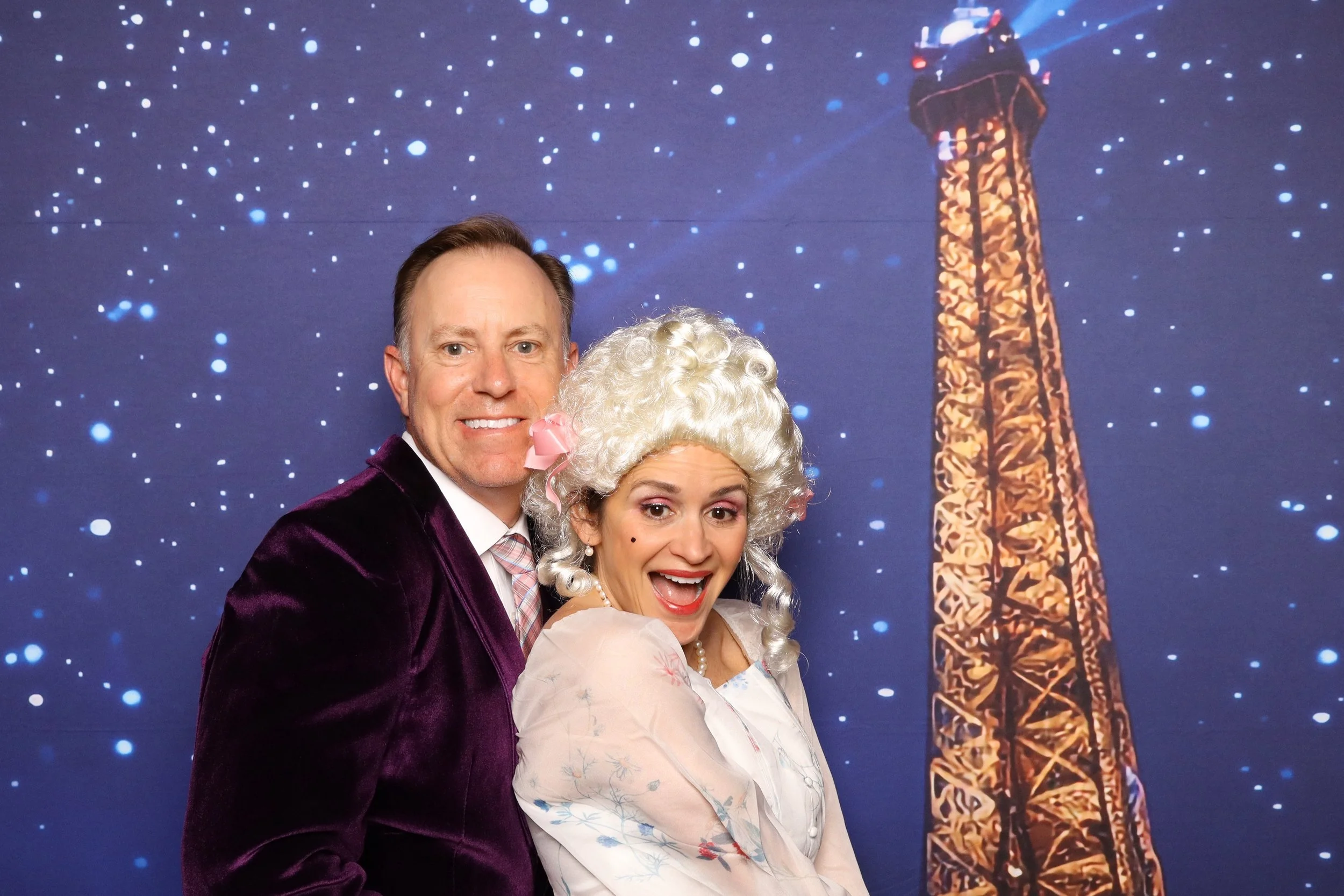 Two adults in costumes smiling in front of a starry background with an illustration of the Eiffel Tower.
