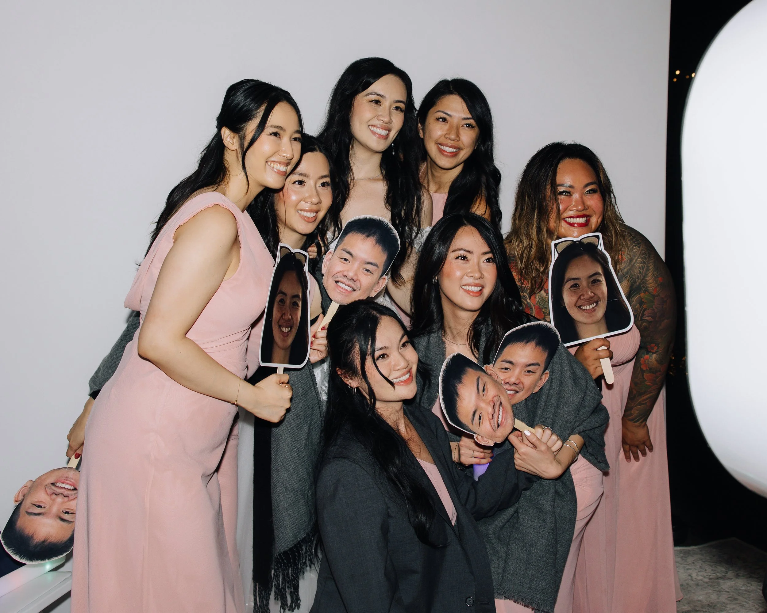 Bride and wedding guests posing together for a photo booth portrait against a white backdrop.
