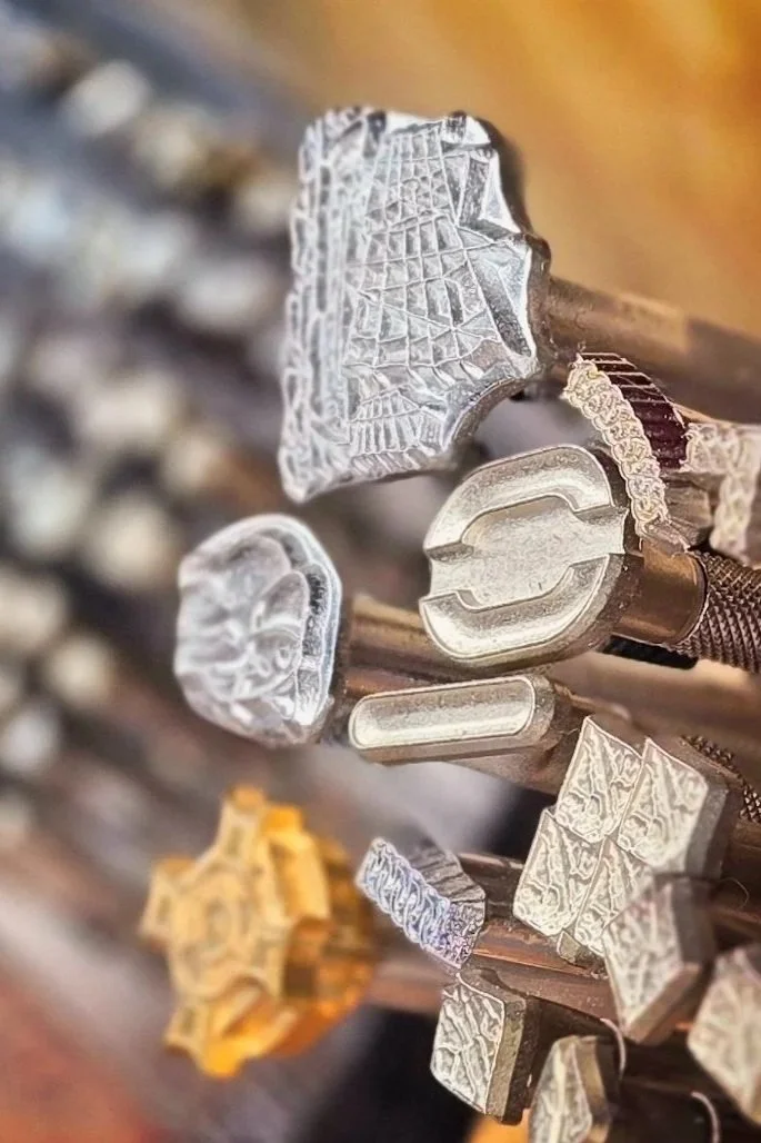 Close-up of leather stamps in various shapes and sizes, arranged on a wooden rack.
