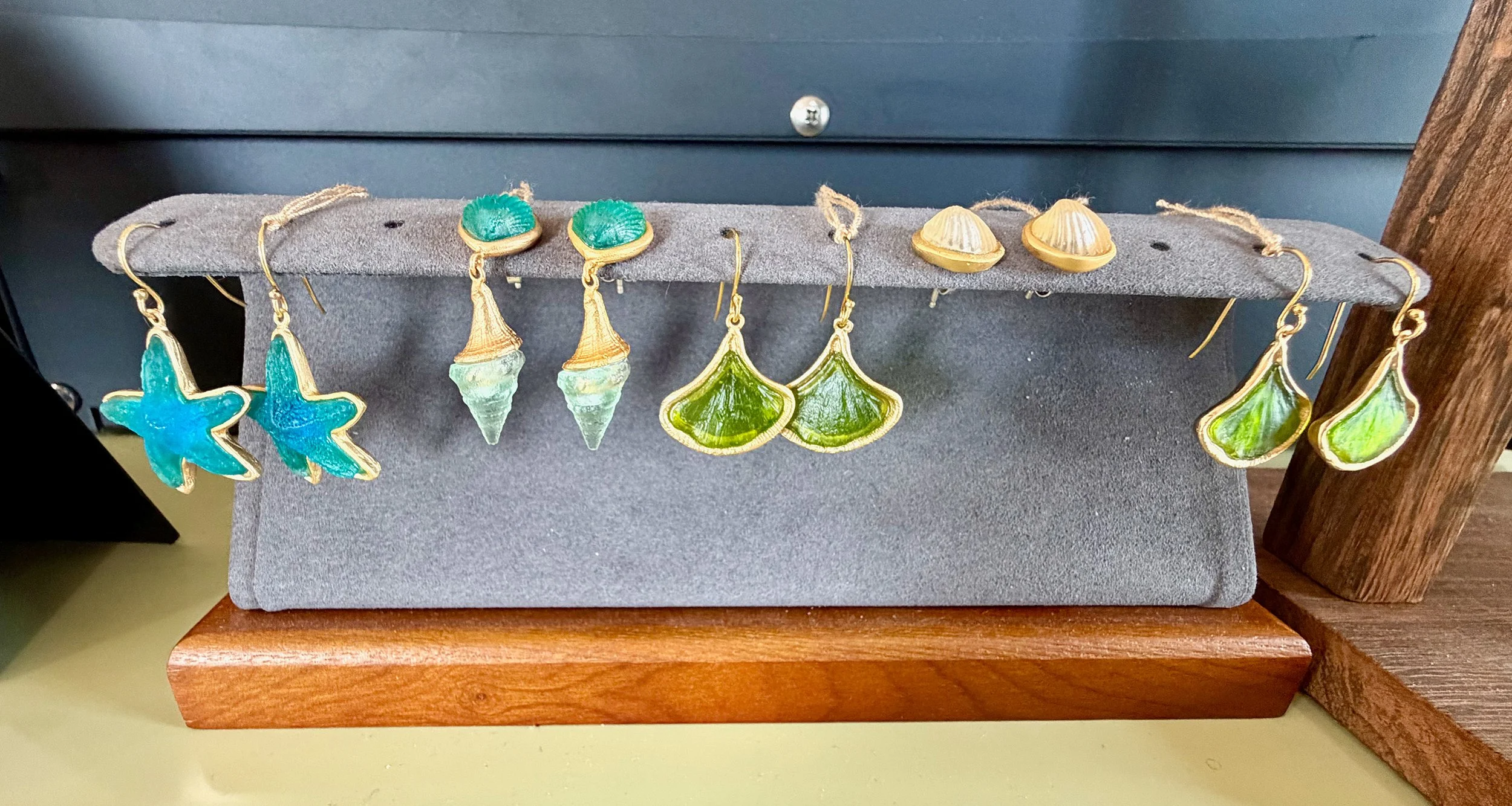 Set of colorful earrings resembling sea creatures and shells displayed on a gray jewelry holder.
