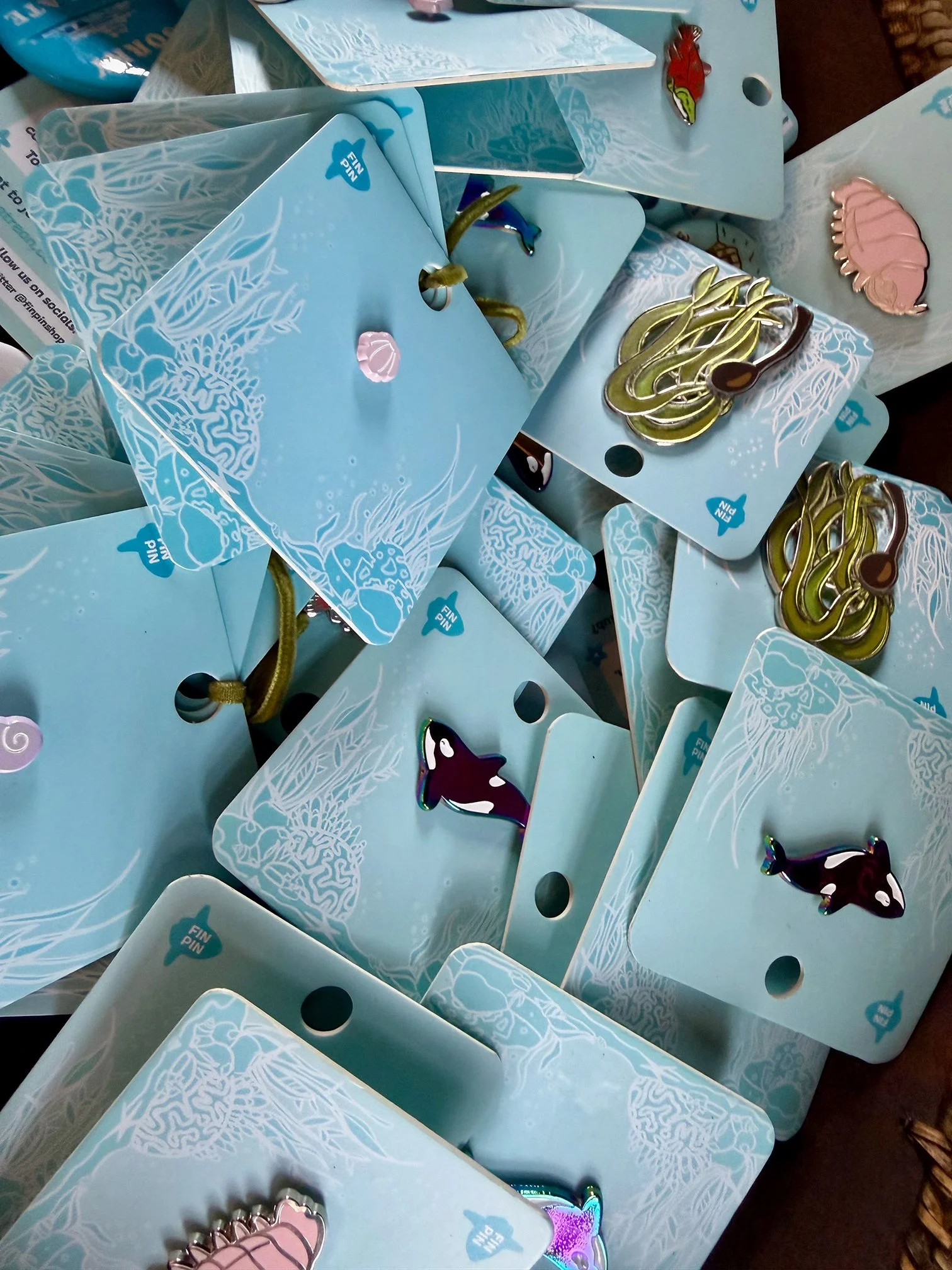 Multiple light blue cards with white coral and wave designs, each attached to a gold string, some featuring shark and dolphin stickers and a pink seashell sticker.