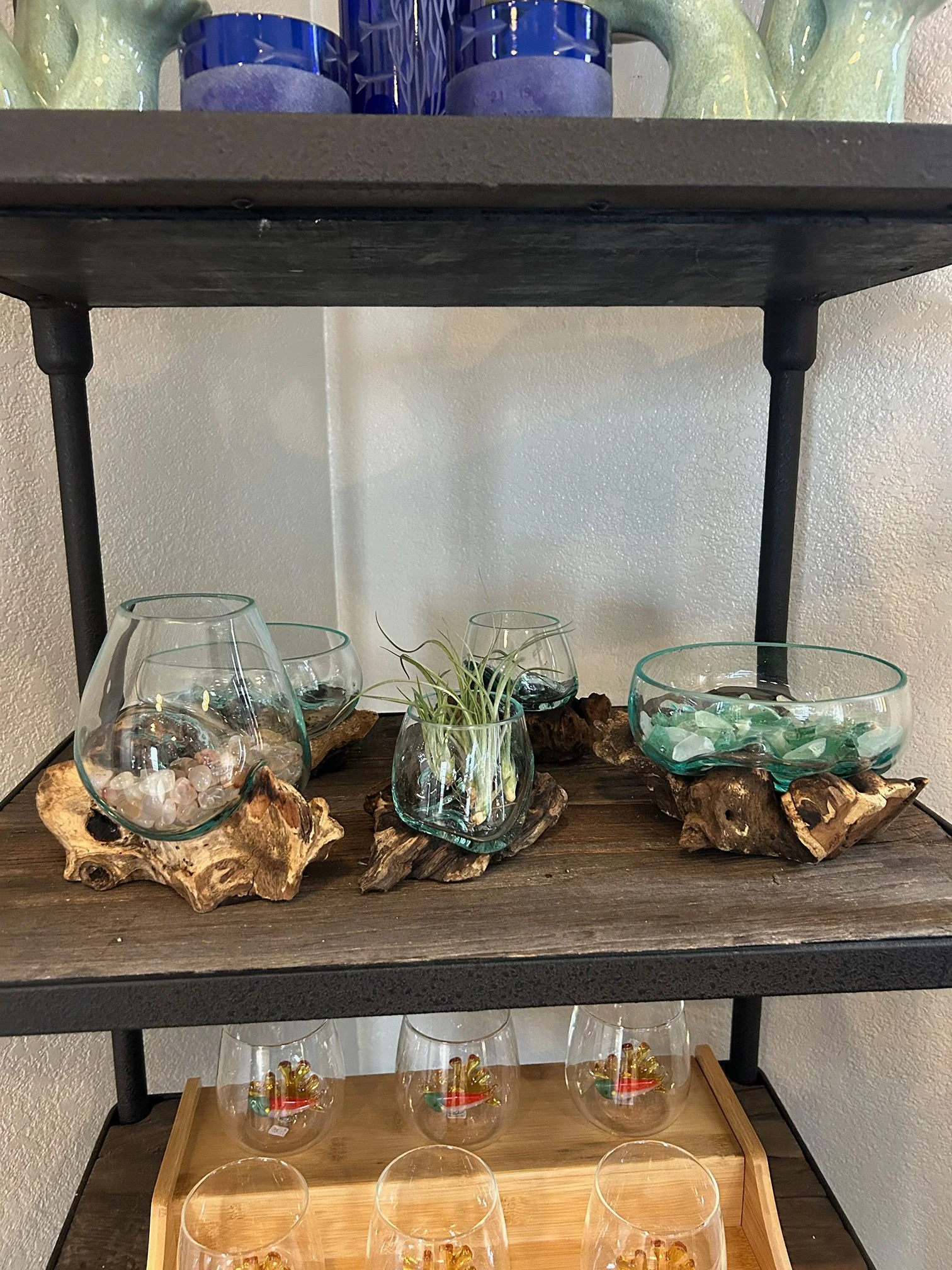 Display shelf with decorative glass bowls filled with shells, stones, and sea glass on wooden and metal stand.