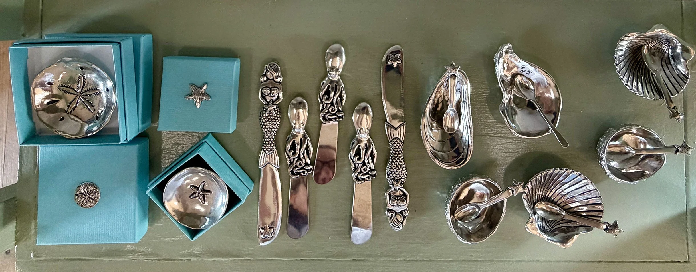 Collection of silver animal-shaped and ocean-themed decorative items, including bowls, spoons, and boxes, with starfish and fish designs, displayed on a green surface.