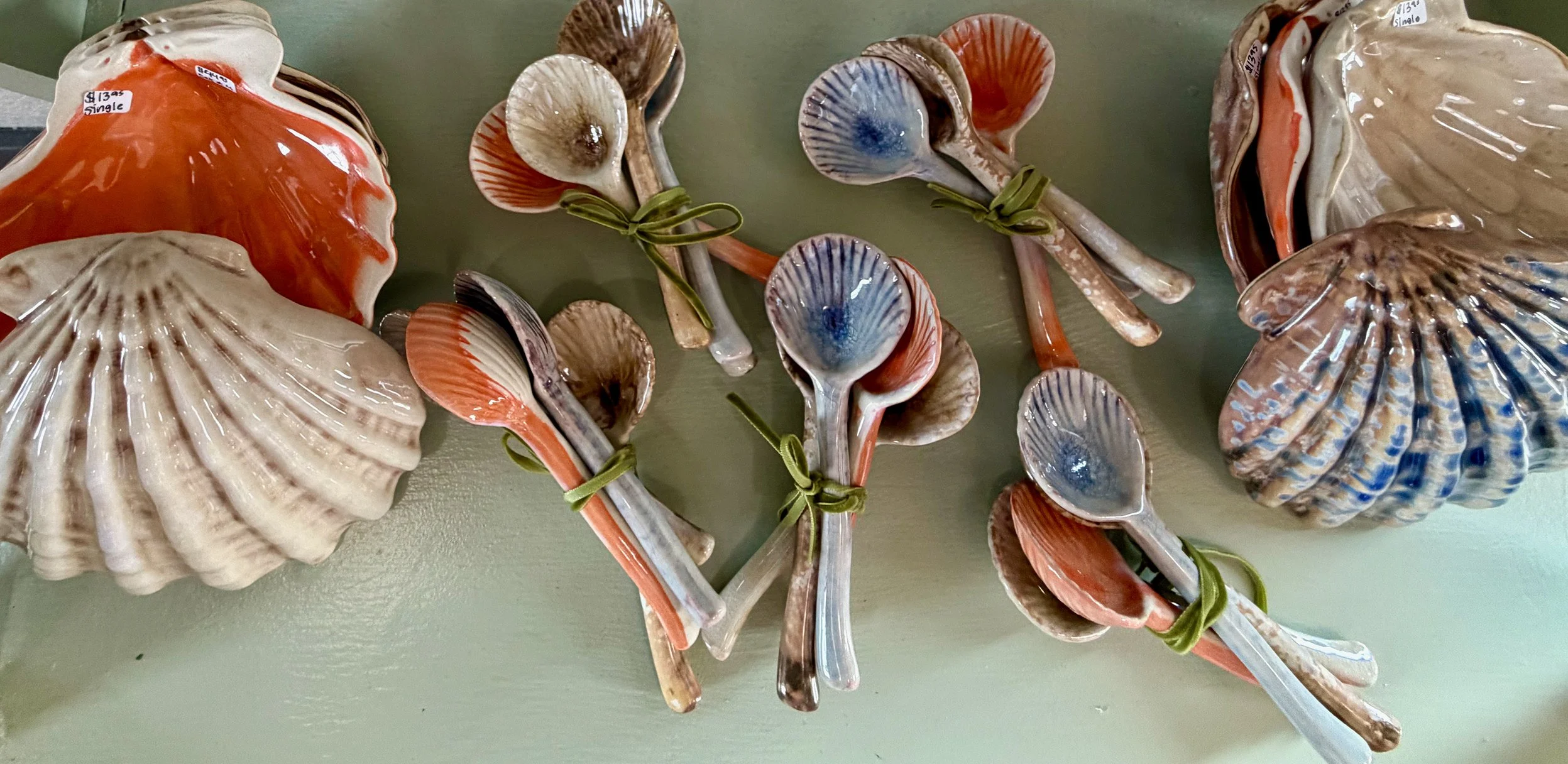 Set of decorative seashell and spoon wall hangings with coral-colored and blue accents, tied together with green ribbons, on a green wall.