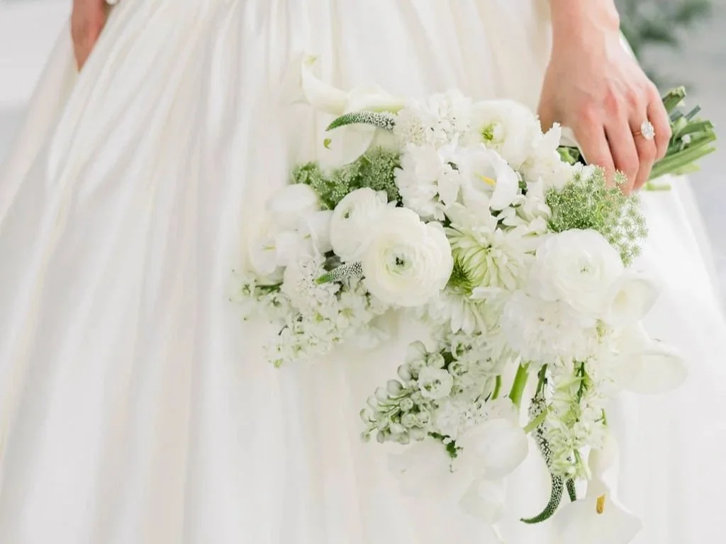 A person in a wedding dress holding a cascading white flower bouquet.