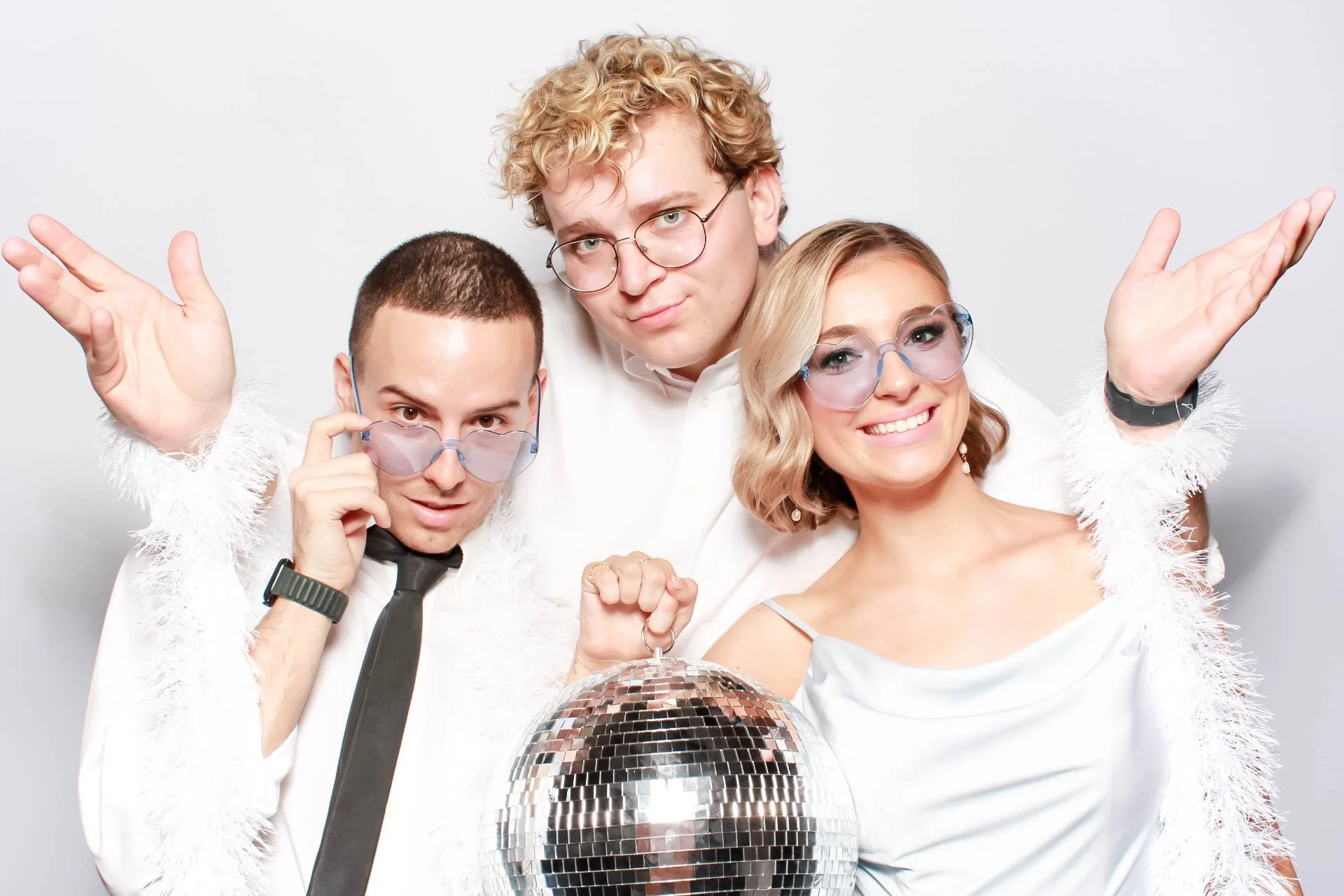 Group of four young adults in party attire posing with a disco ball and dancing in front of a plain white background.