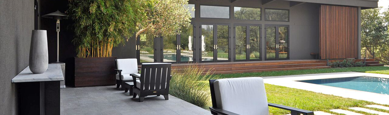 Modern backyard patio with outdoor chairs, a pool, and a house with large glass doors and windows.