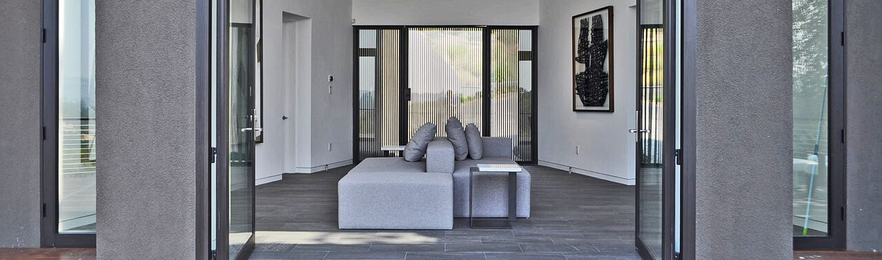 Modern living room with large sliding glass doors, gray sectional sofa, artwork on white walls, and dark wood flooring.