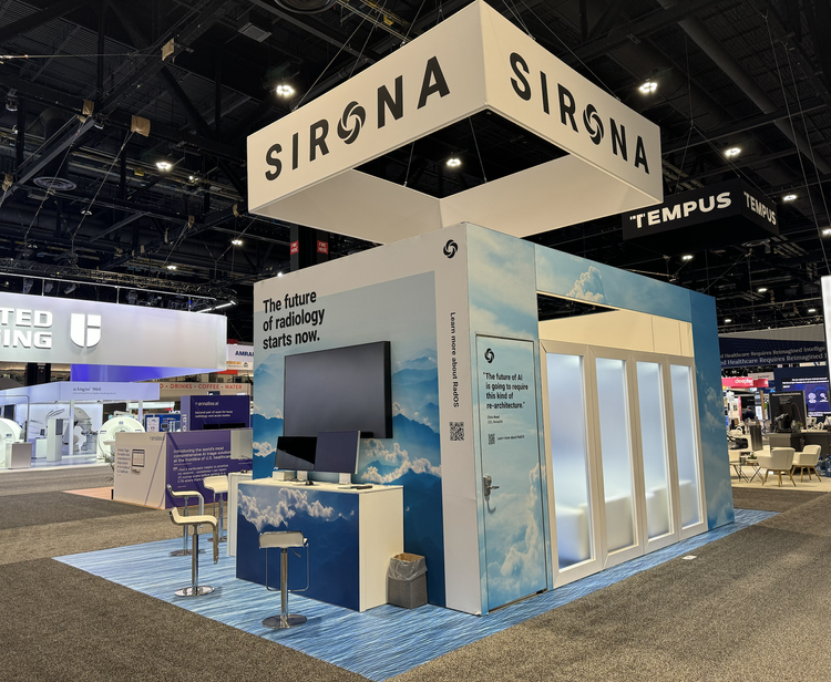 Exhibit booth with lighting blue sky cloud design, large screen, seating area, and signs that say 'The future of radiology starts now' with prominent 'SIRONA' banners overhead at a trade show.