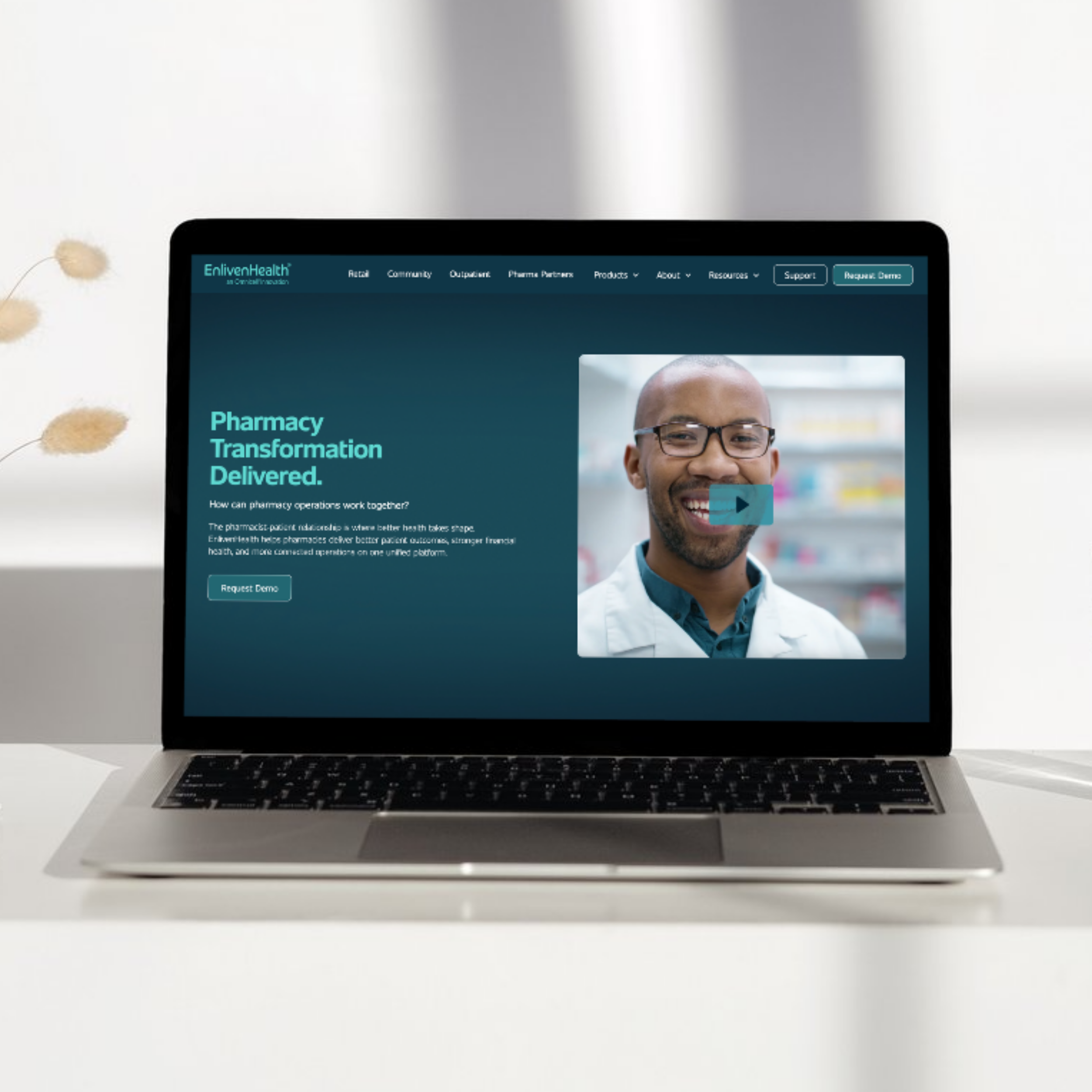 A laptop on a white desk with a webpage open, showing a man in glasses smiling.