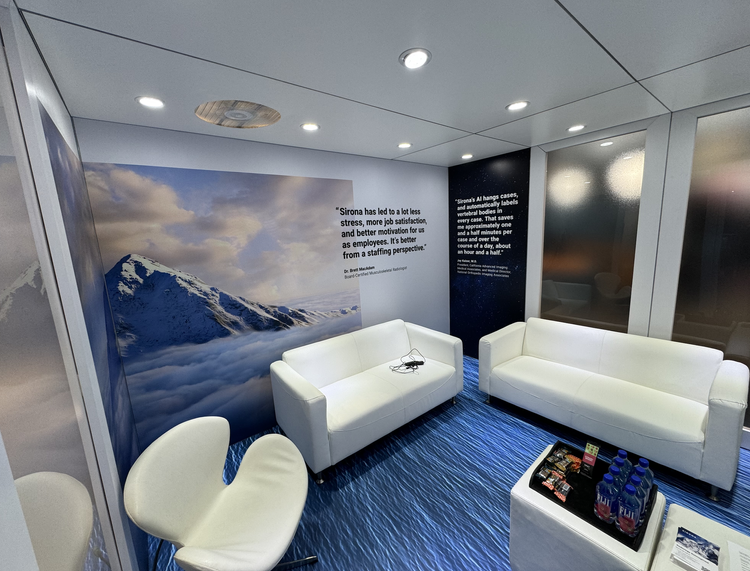 A modern office lounge with white sofas, a white chair, and a small table with bottled water and snacks. The wall features a large snow mountain landscape with clouds and a quote about leadership and employee satisfaction.